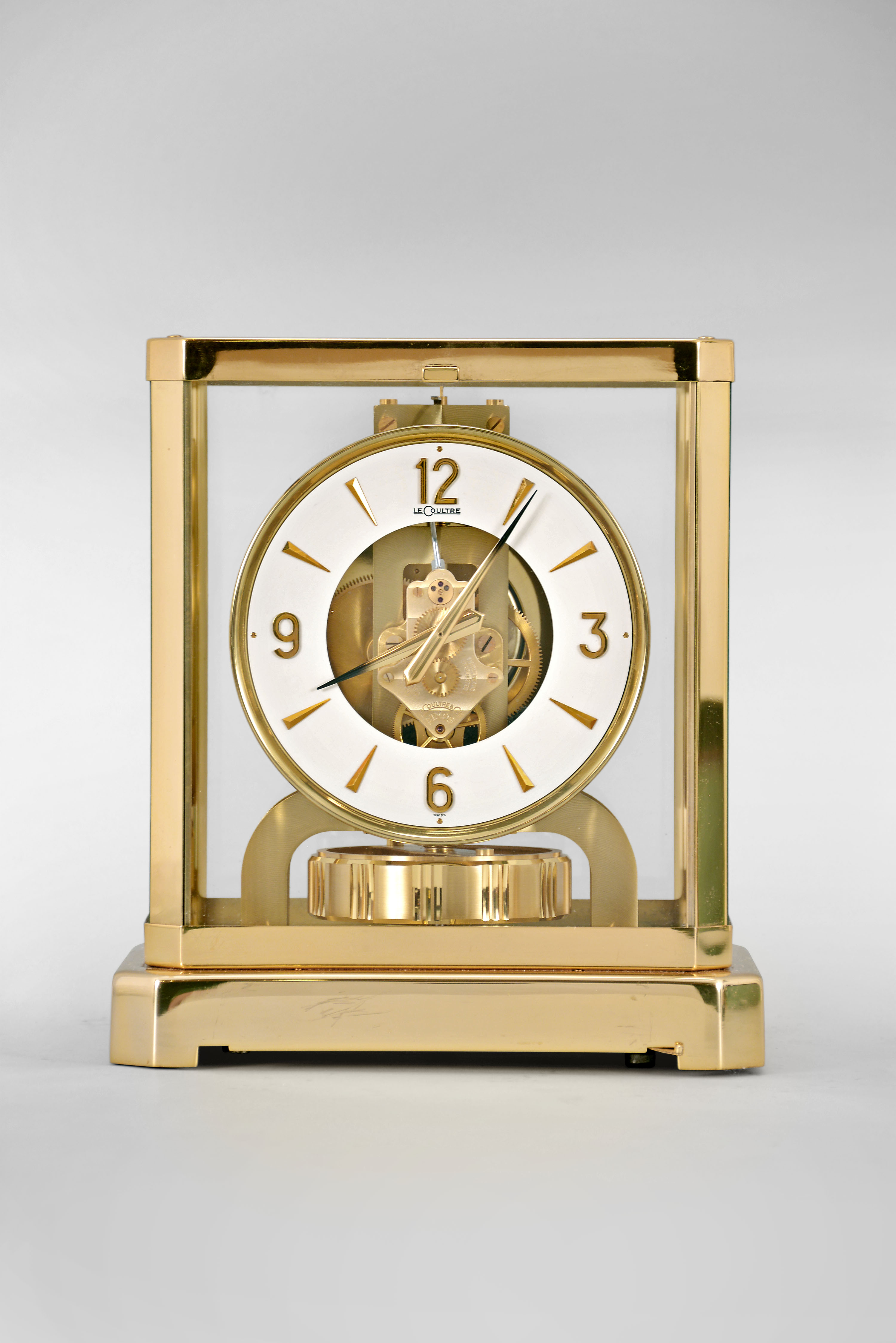 Jaeger- LeCoultre, Switzerland, "Atmos" clock, 15 jewel movement, gilt torsion pendulum, round white painted dial with applied gilt Arabic numerals and arrow markers, gilt hands all contained in a glazed rectangular case with removable front panel, serial #245342. — Antique Clocks Price Guide