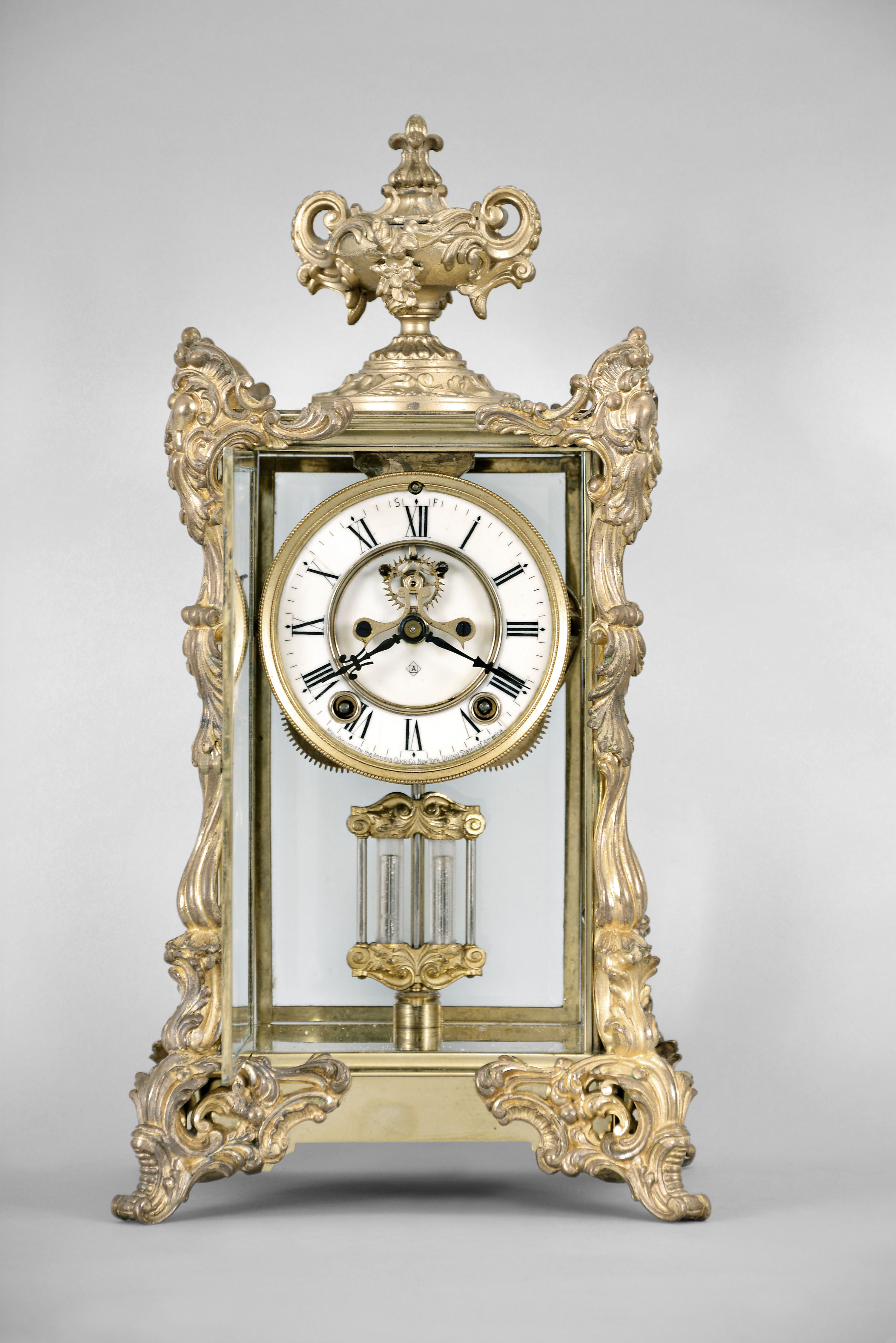 Ansonia Clock Co., New York, "Marchioness" crystal regulator with a spring driven 8 day time and half hour strike (rack and snail) movement (visible escapement) in a polished brass case with rich gold ornaments. — Antique Clocks Price Guide