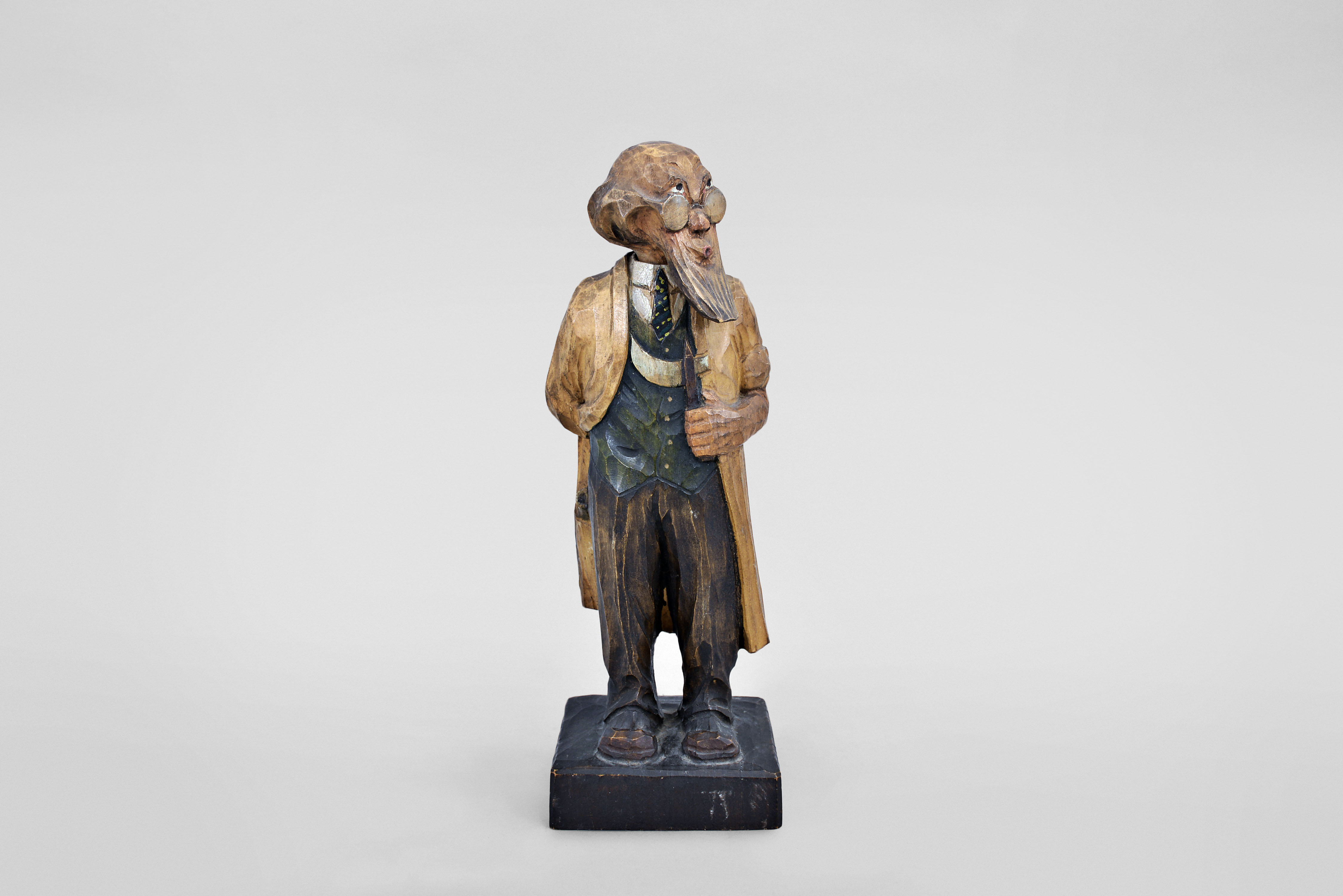 Karl Griesbaum, Triberg, Germany, "Surgeon" whistling figure, spring driven brass movement powering air bellows, a cam-driven slide whistle, and swinging head motion, all within a hand carved wooden figure depicting a bespectacled man in a long coat holding knife in one hand while whistling a tune. — Antique Clocks Price Guide