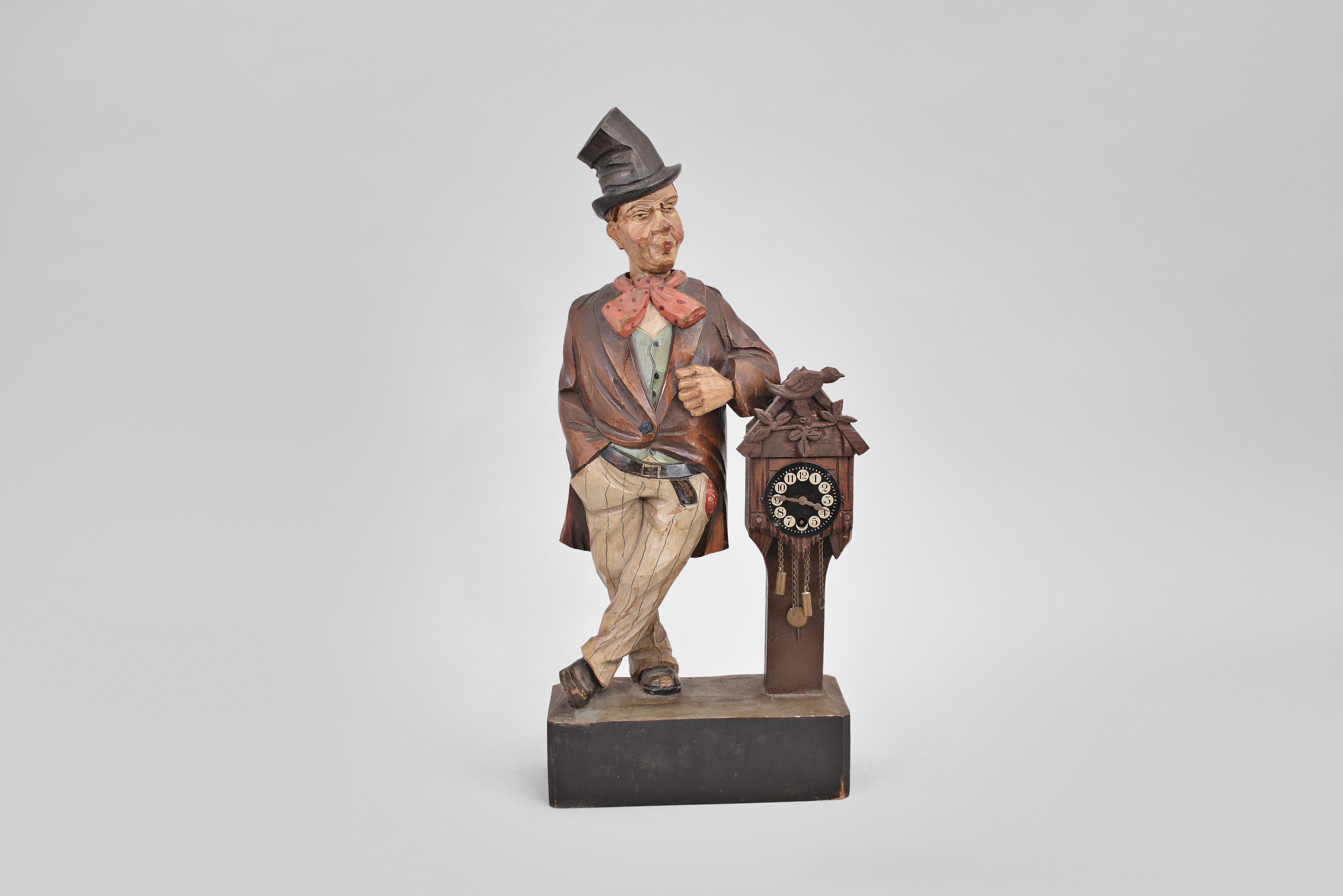 Karl Griesbaum, Triberg, Germany, "Drunkard" whistling figure, spring driven brass movement powering a bellows, a cam-driven slide whistle, and head turn motion, enclosed within a hand carved wooden figure of a man in a top hat leaning on a small working clock, a bottle tucked in his hip pocket. — Antique Clocks Price Guide