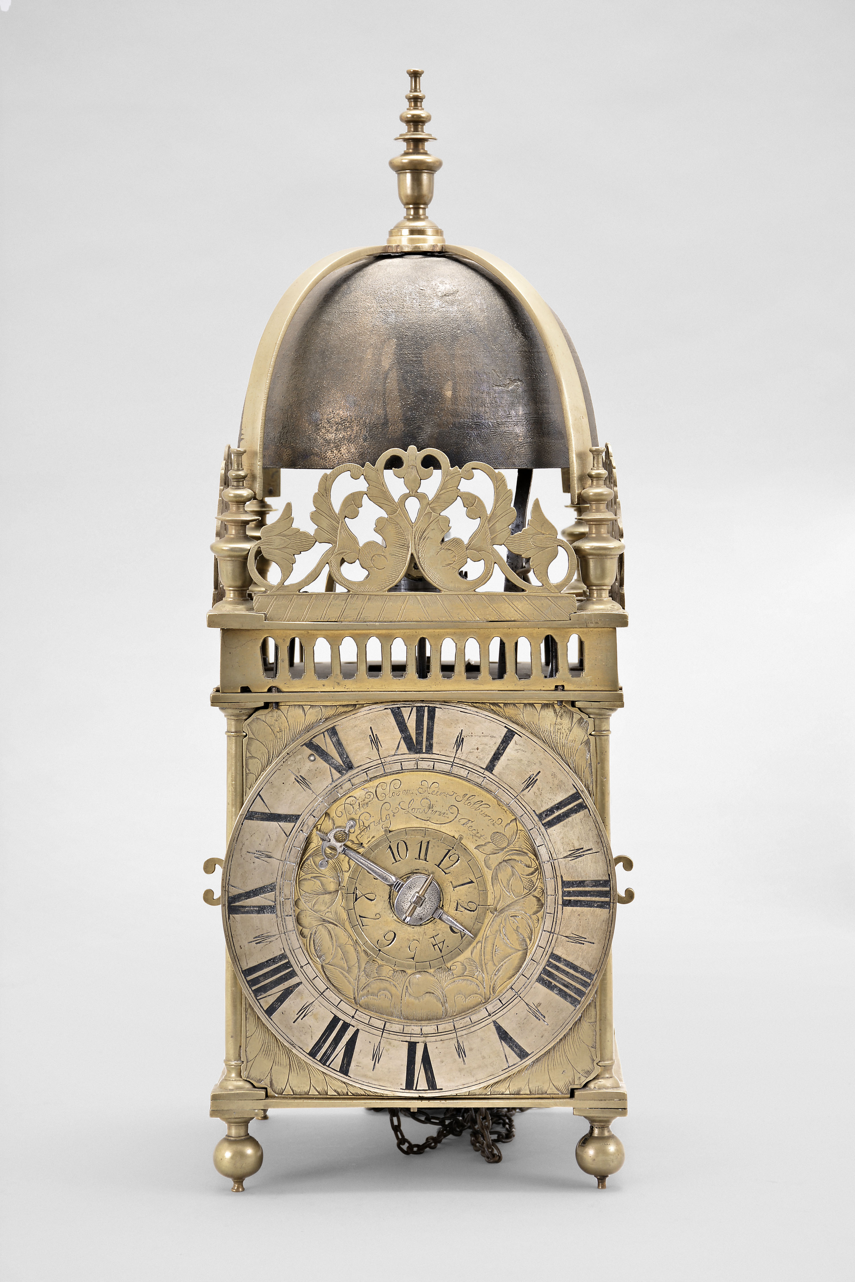 Peter Closon, London, a mid 17th century striking lantern clock, the brass case with turned, tapered columns at the corners, with ball feet and ornate urn finials, the top with arcaded brass gallery fixed to the top plate, and with a second top above, screwed to the lower plate and located by pins formed from extensions of the columns, three sides with engraved, foliate frets, and top with brass bell strap with finial and large bell, dial plate with foliate engraved corners, the center with engraved tulips, and signed "Peter Closon Neere Holburn Bridge Londini Fecit", silvered brass chapter ring with roman numerals and matchstick flower half hour markers and single, cut steel hand, movement with crown wheel escapement and count wheel striking, crown wheel made of steel instead of the more ususal brass, contrate wheel with three spoke crossing dovetailed to the rim, hour wheel and ratch with matchstick man marks — Antique Clocks Price Guide