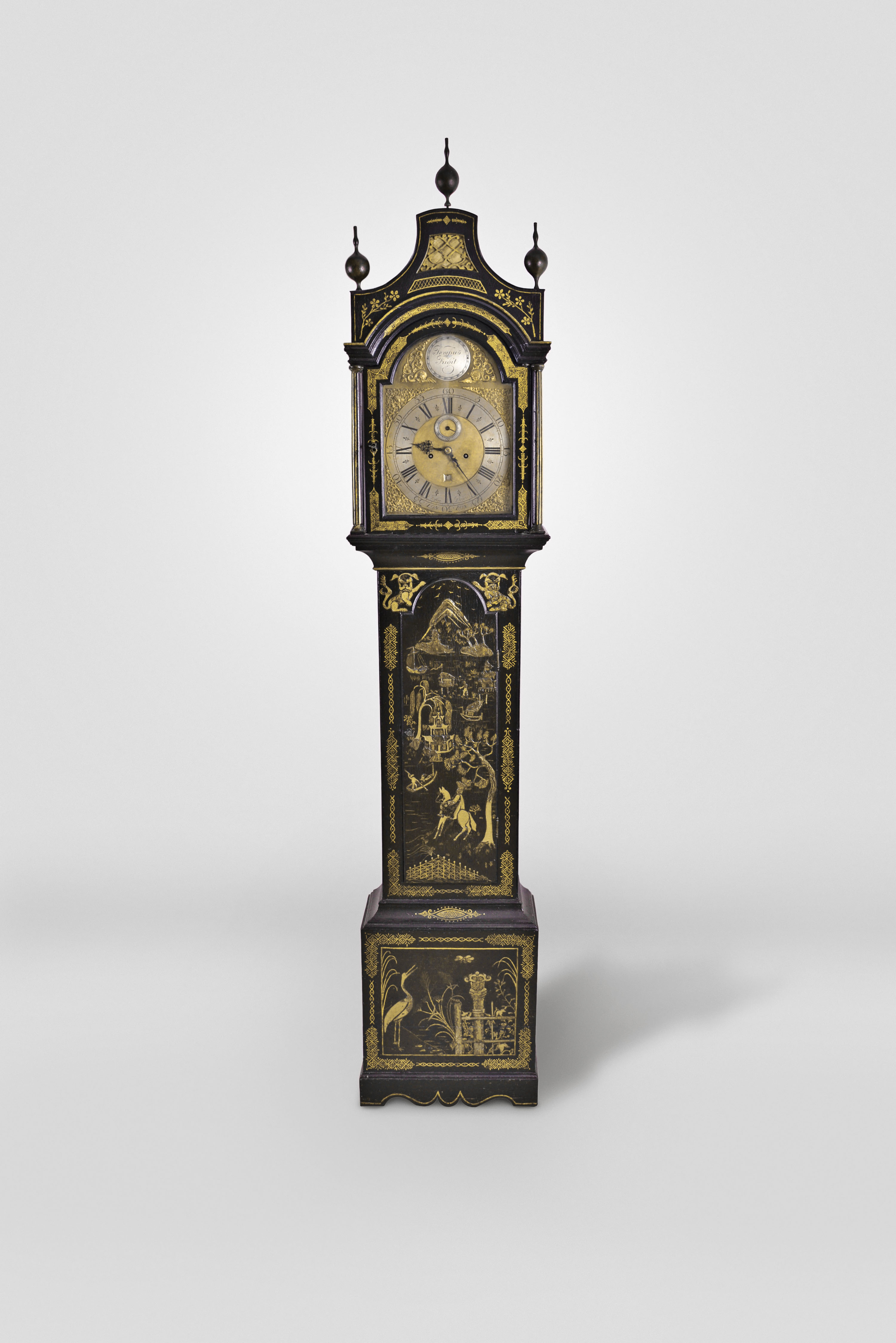 John Dewe, London, England, tall clock, 8 day, time and bell strike, weight driven movement in an ebonized and japanned pagoda top case with three finials resting on a base with a cutout skirt. The brass dial has seconds bit, calendar, silvered chapter ring, boss engraved "Tempus Fugit" flanked by two brass dolphin spandrels, corner spandrels with female heads, signed by maker below 6. — Antique Clocks Price Guide