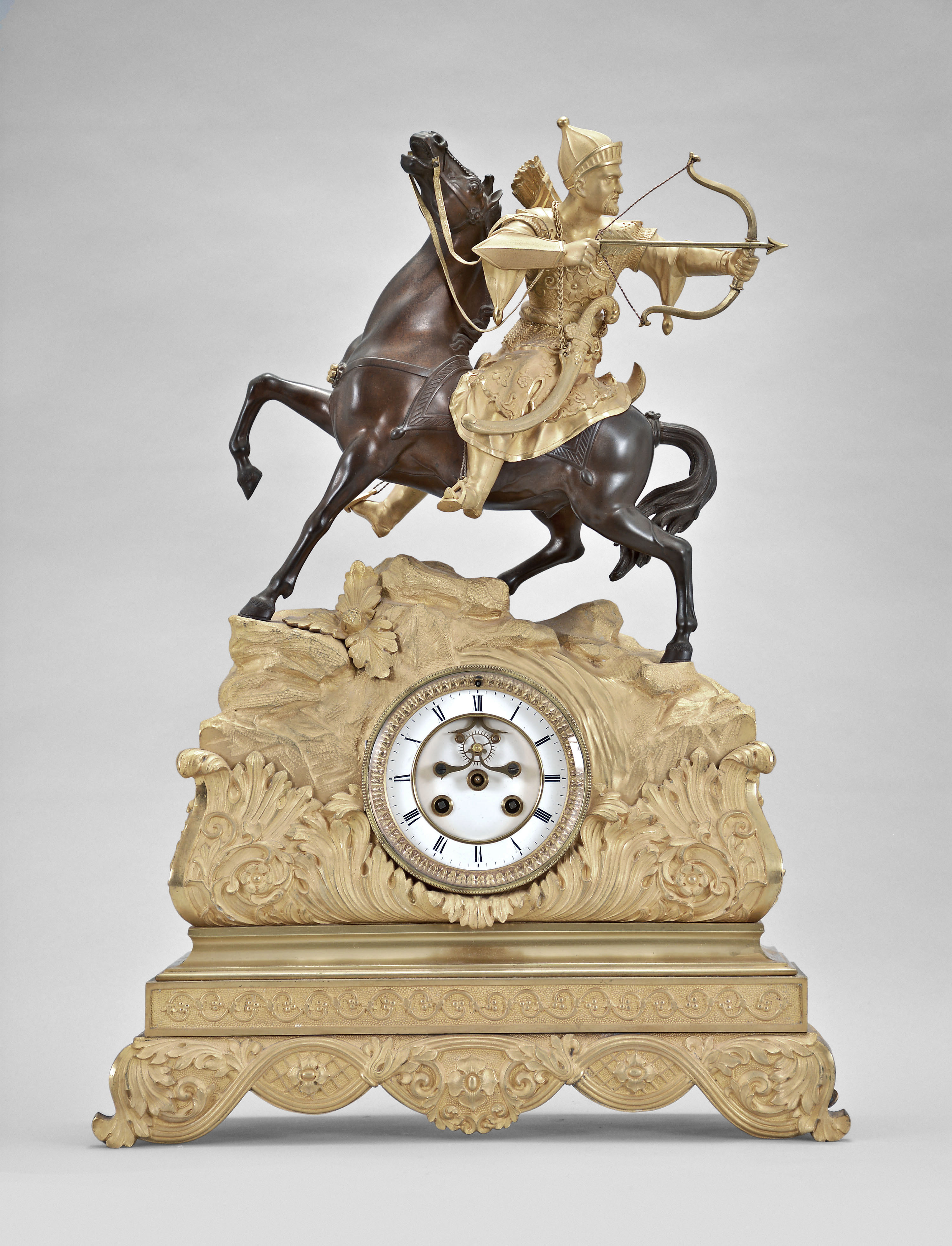 France, a gilt and patinated bronze figural mantel clock, the case replete with symmetrically arranged acanthus and other naturalistic top, the top with a rocky landscape and a Turkish archer wearing armor, astride a reddish brown patinated horse, the horse with head and one leg raised, the figure looking backward, his bowstring taut, and ready to release an arrow, Roman numeral white enamel dial with open escapement, 8 day, two train pendule de Paris movement — Antique Clocks Price Guide