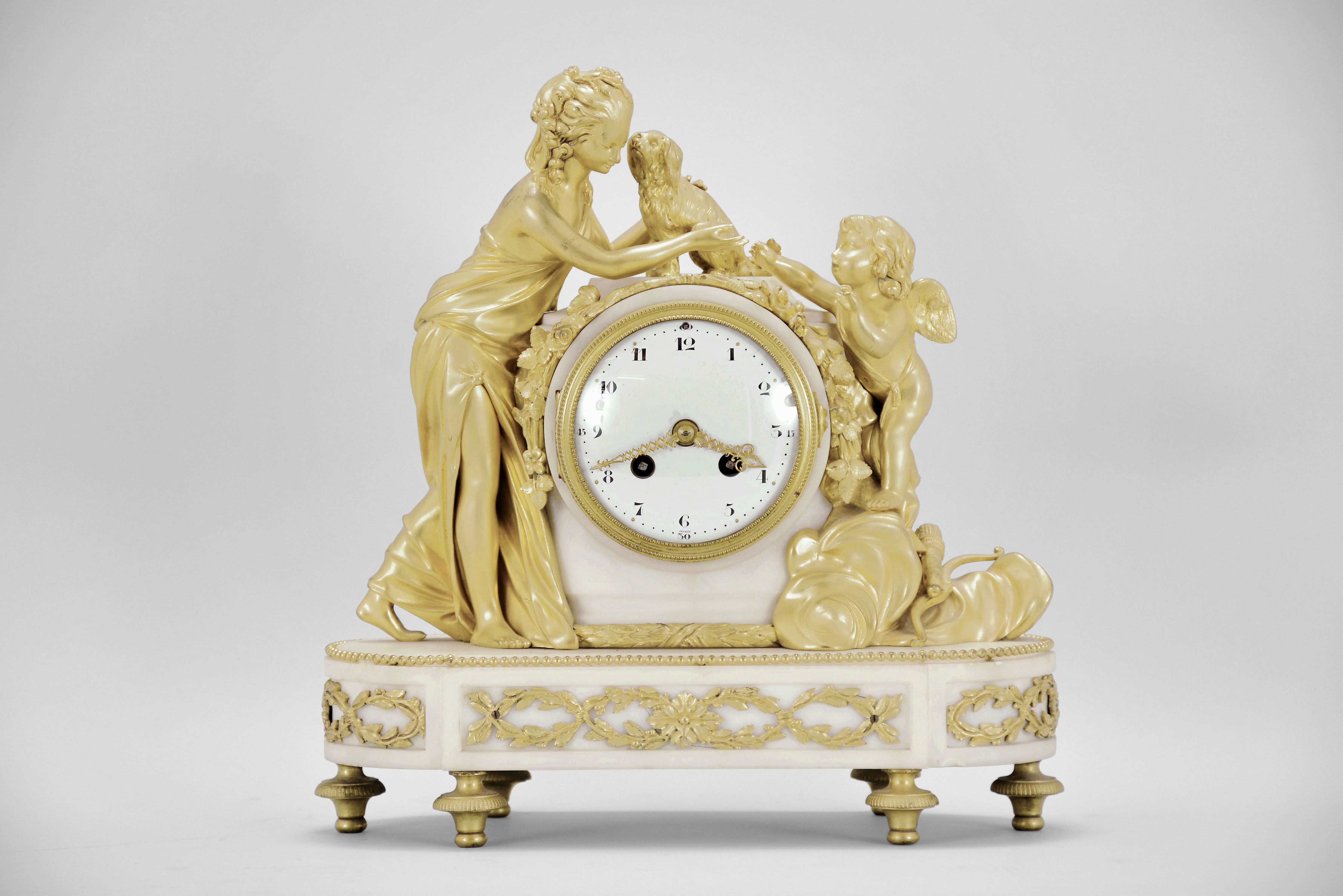 Samuel Marti, Paris, France, figural mantel clock, 8 day, time and strike, spring driven pendule de Paris movement in a white marble case on turned brass feet with applied gilt ornaments, supporting gilt figures of a woman, dog, and Cupid, white convex enamel dial with Arabic numerals and gilt fleur-de-lis hands. — Antique Clocks Price Guide