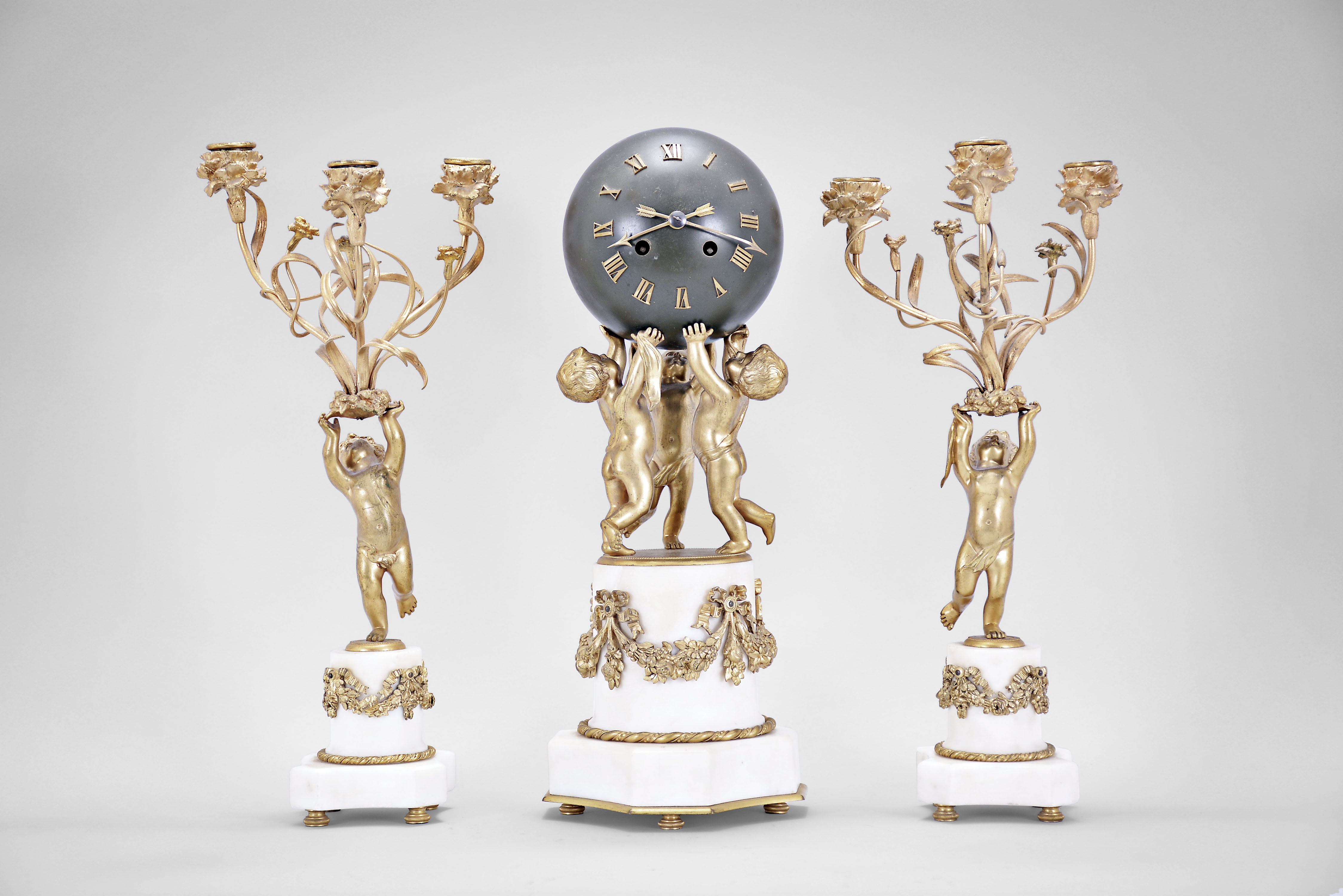 Japy Freres, Paris, France, three piece mantel garniture set, 8 day, time and strike, spring driven movement with platform escapement, the case with three putti supporting a sphere with applied roman numerals and arrow hands resting on a marble base with gilt cast appliques and two matching side pieces with putti holding aloft the candleabra — Antique Clocks Price Guide