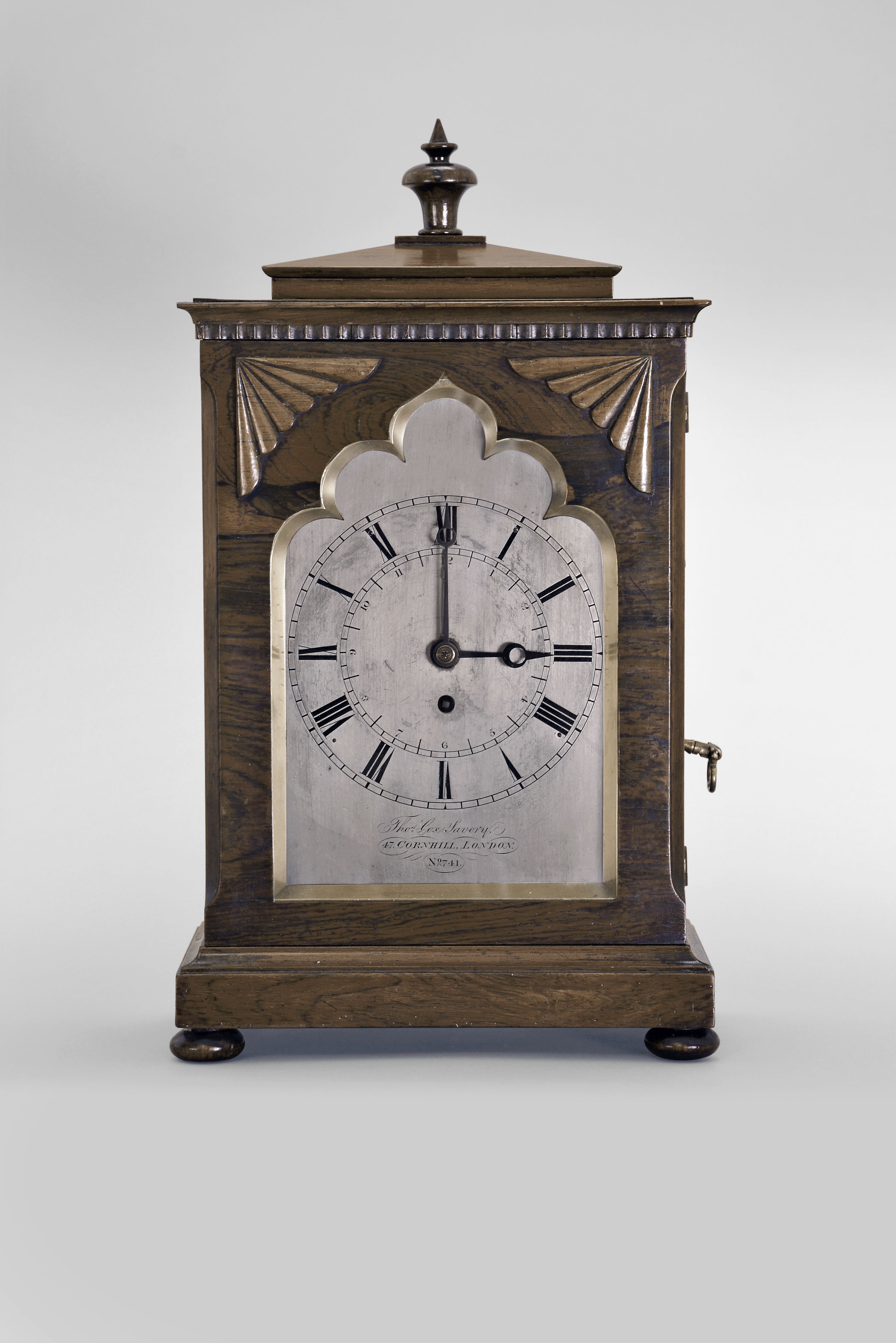 Thomas Cox Lavory, 47 Cornhill, London, mantel timepiece, 8 day, time only with pull alarm, spring driven fusee movement in a rosewood veneered case of Gothic design with stepped molded base and top, applied wood ornaments on the door front with foil arch window, silvered dial engraved as above, Roman numeral dial, and blued steel moon hands. — Antique Clocks Price Guide