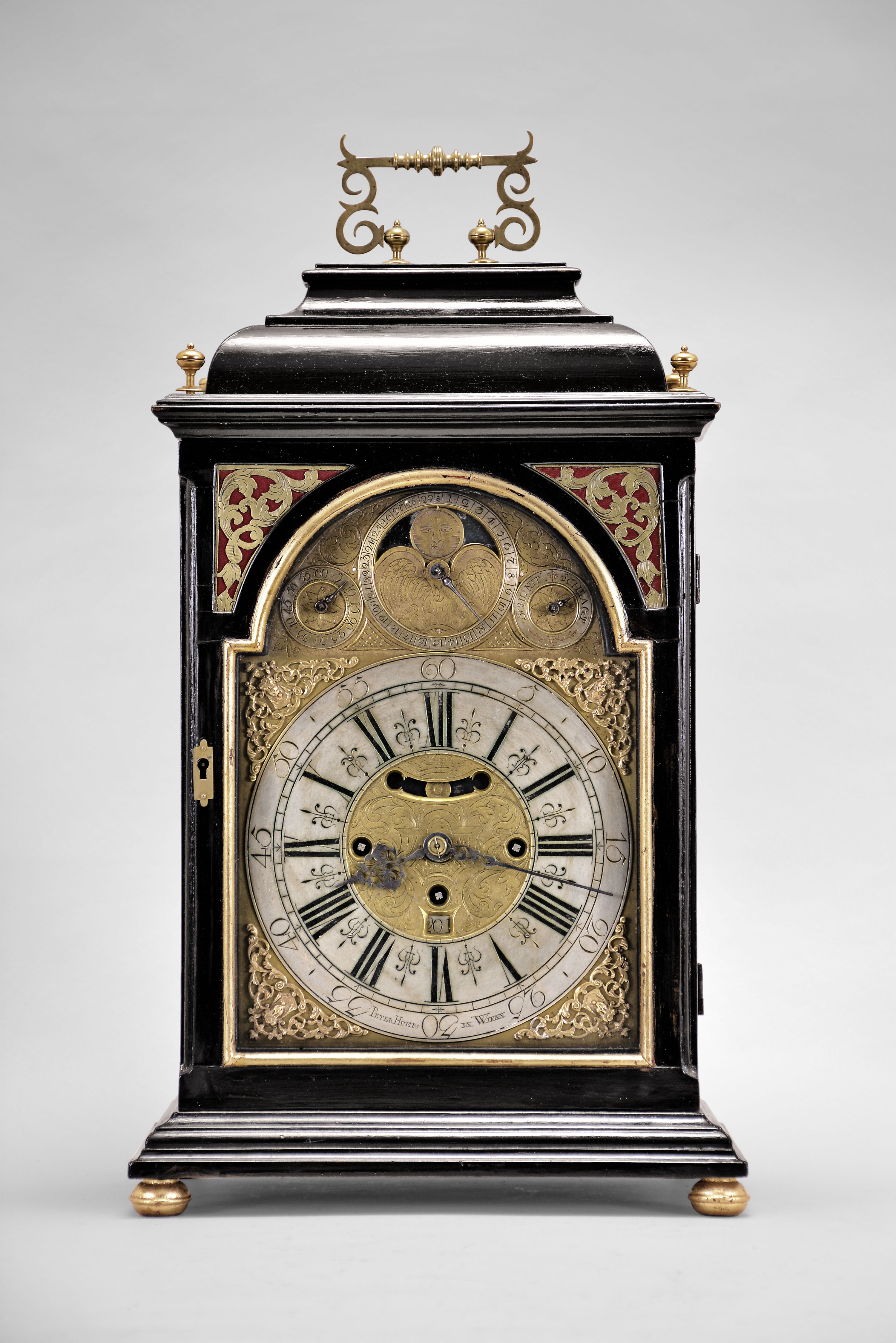 Peter Humps, in Wienn, a mid 18th century, grand sonnerie striking bracket clock with date and phases of the moon, ebonized case with molded base on turned, gilt feet, the arched, gilt lined, glazed door with textile backed engraved frets at upper corners, case sides also with glazed, gilt lined, arched windows and sound frets, the caddy top with ornate carrying handle, and flanked by four turned finials, brass composite dial with roman numeral chapter ring and arabic five minute markers, center with foliate engraving and date aperture above 6:00, and cutout to view mock pendulum below 12:00, corners with cast spandrels, and the arch with regulator, strike/ silent control, and moon phase display, blued steel hands, 30- 60 hour, three train movement with engraved backplate, decorated crutch, turned pillars with central knop, crown wheel escapement, fusee for time train, Viennese striking, and repeating the last hour and quarter on demand, and small, engraved brass pendulum bob with steel rod — Antique Clocks Price Guide