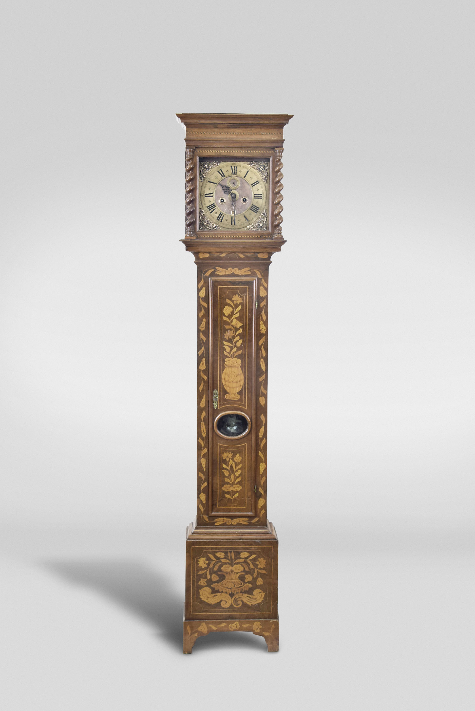 Joan. Klock, Amsterdam, Netherlands, tall clock, 8 day, time and strike with alarm, weight driven movement in a marquetry inlaid mahogany case with flat top and twist columns flanking hood and lenticle glass for pendulum on trunk door resting on bracket feet. The brass dial has Roman numeral chapter ring, calendar aperture and seconds bit with maker's signature below 6. — Antique Clocks Price Guide