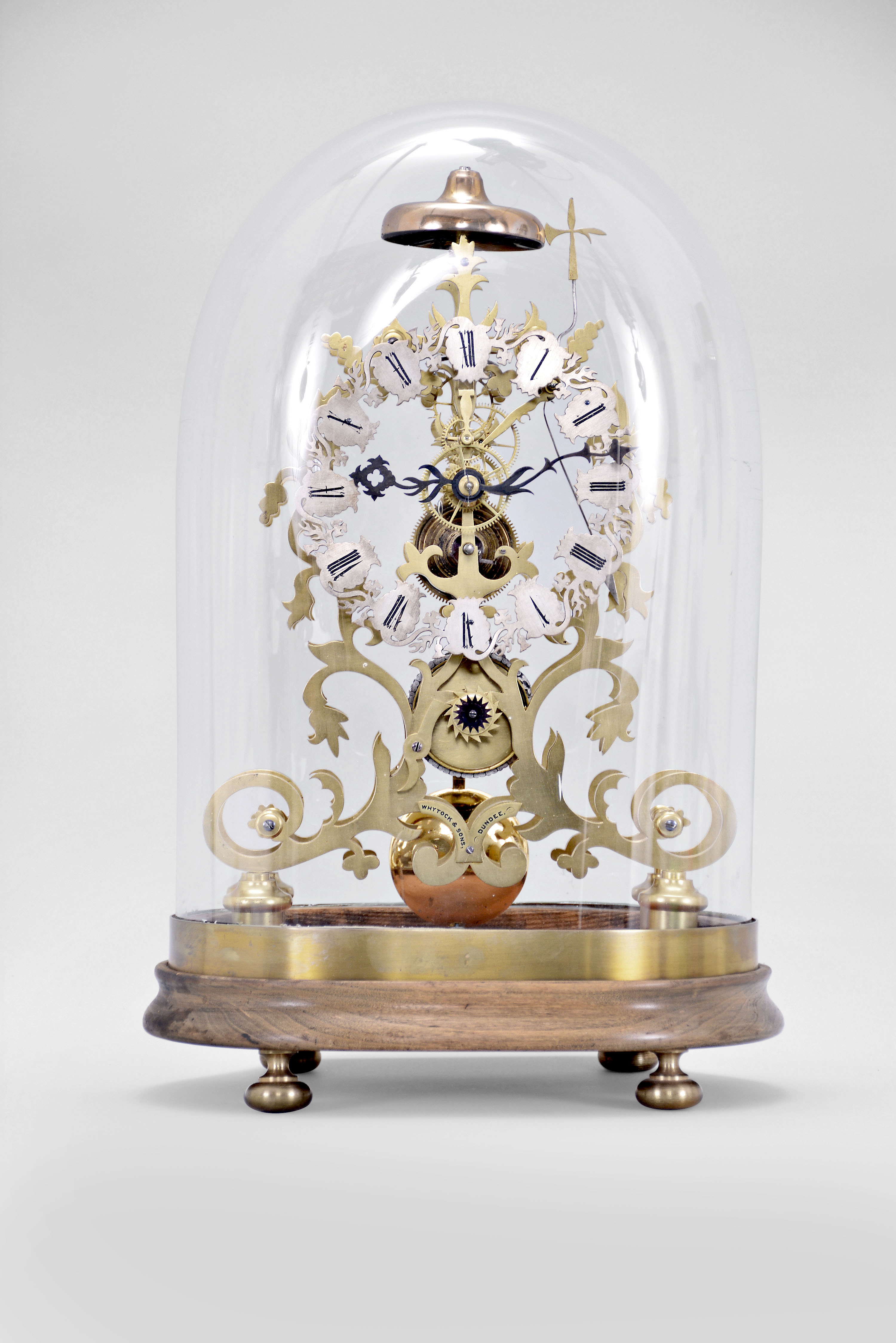Whytock and Sons, Dundee, a mid 19th century skeleton clock with passing strike, the frames fretted in the form of vines and foliage topped with a finely finished bell, the fusee movement with recoil escapement and inline wheelwork with five spoke crossings confined to the center of the frame and so allowing for a very open design, the silvered dial with gothic roman numerals also following the frame design, and incorporating thistle, vine and shamrock motifs, fancy blued steel hands and heavy brass clad pendulum, beneath an oval glass dome with conforming wooden base — Antique Clocks Price Guide