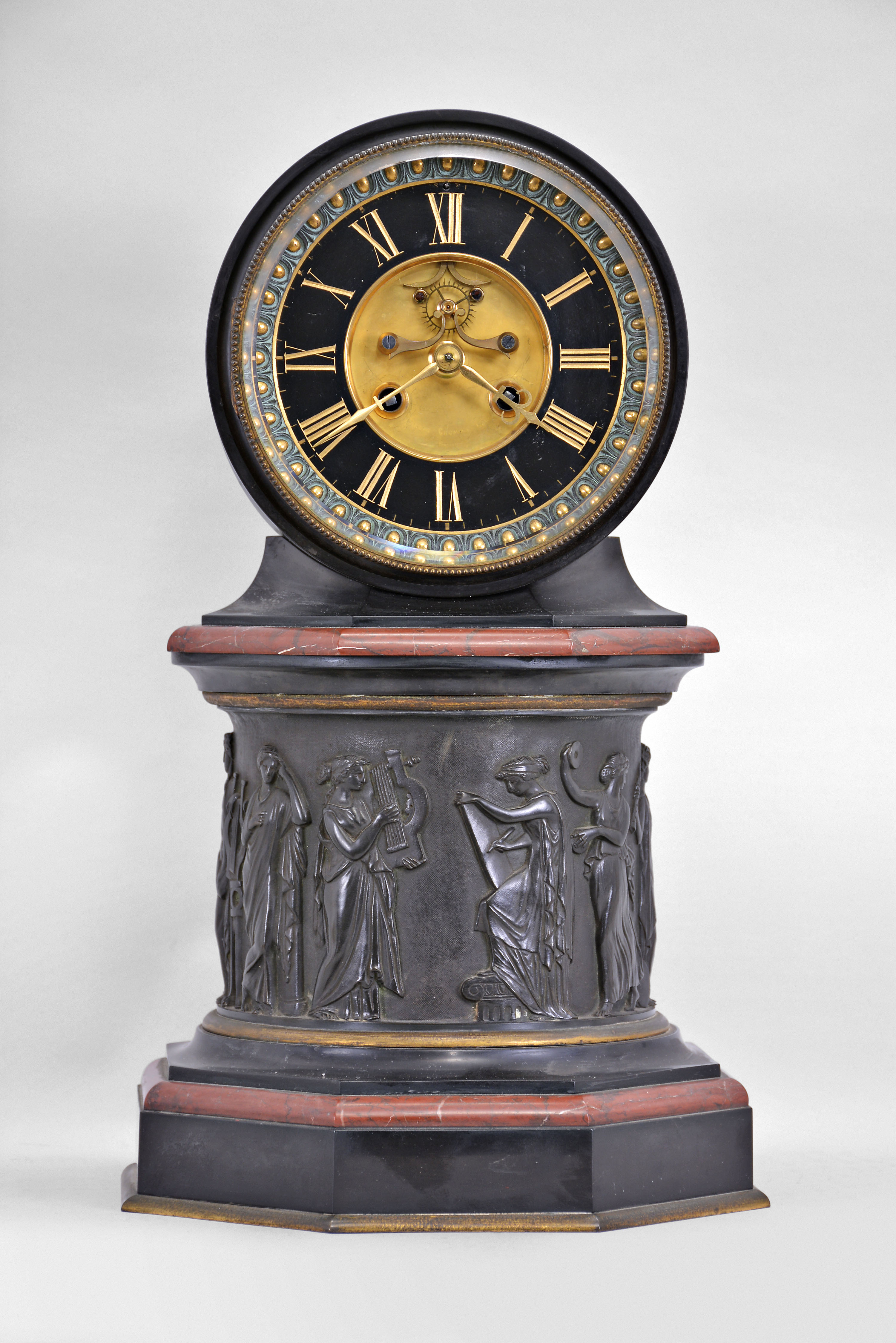 E. Maurice and Co., Paris, France, for Shreve, Crump &amp; Low, Boston, mantel clock, 8 day, time and strike, spring driven pendule de Paris movement with visible Brocot escapement on an molded octagonal base with gilt brass and red marble ovolo molding supporting a central column with the Greek muses cast with relief from patinated metal, supporting a molded octagonal capital upon which rests a drum head of black slate holding the movement, bezel, and polished black slate dial with incised Roman numerals and gilt hands. — Antique Clocks Price Guide
