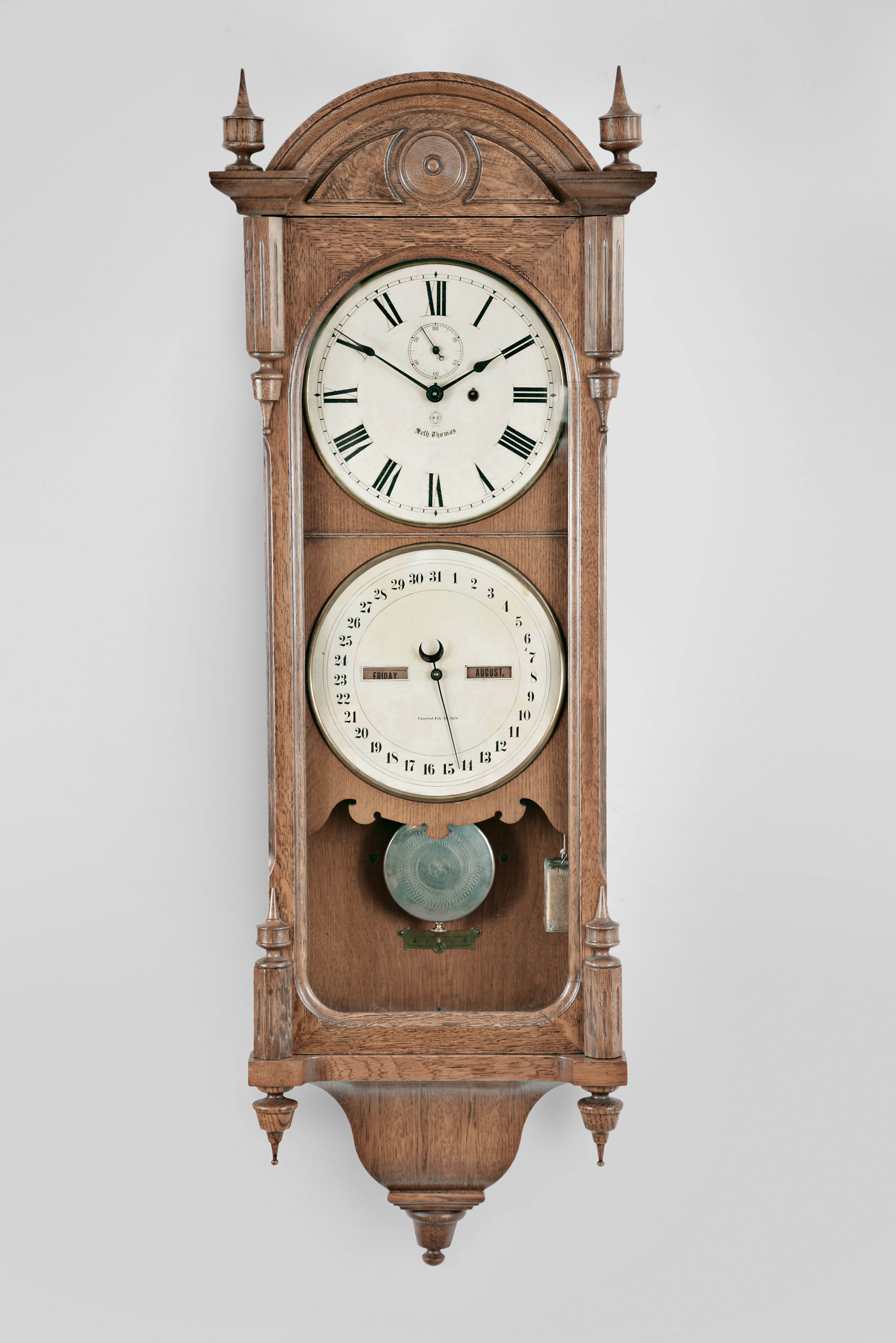 Seth Thomas Clock Co., Thomaston, Conn., "Office Calendar No. 10" hanging clock with a weight driven 8 day timepiece movement, maintaining power, and an R. T. Andrews patented perpetual calendar mechanism in an oak case with burl accents. — Antique Clocks Price Guide