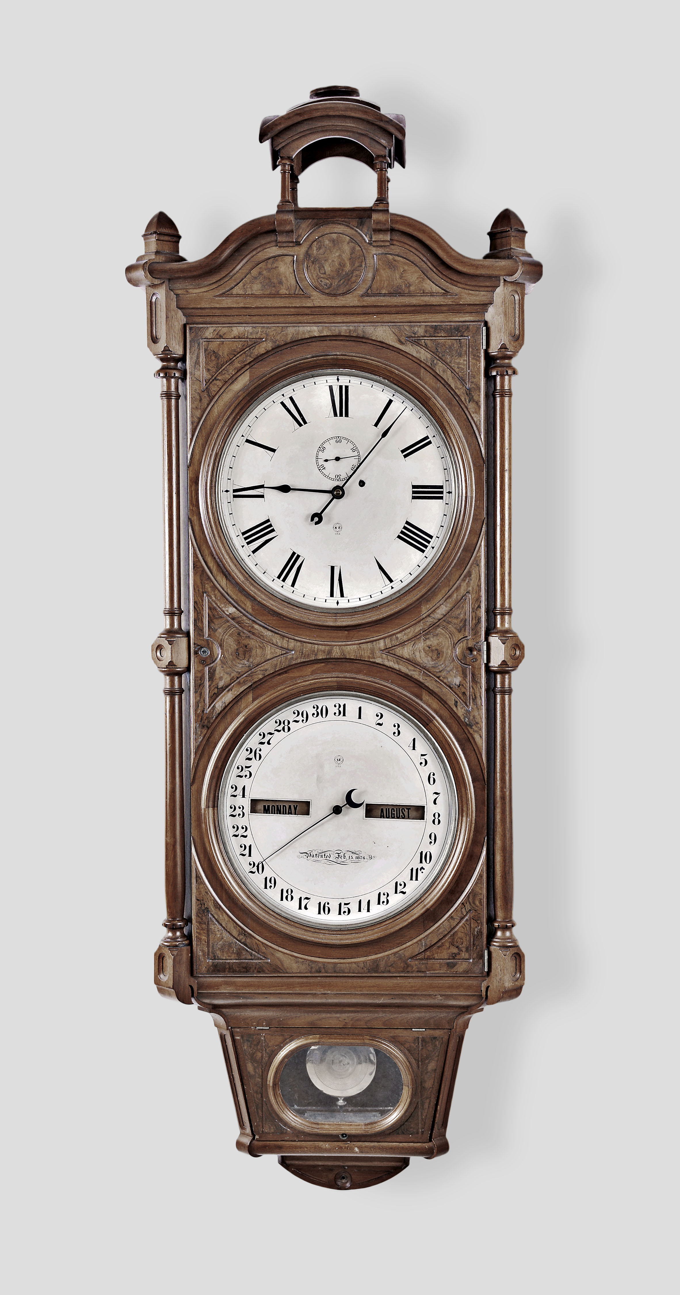 Seth Thomas Clock Co., Thomaston, Conn., "Office Calendar No. 8" wall clock, 8 day, time and perpetual calendar, weight driven movement in a walnut and burl walnut case with canopy top, glazed pendulum aperture and painted metal dials, and damascened pendulum bob — Antique Clocks Price Guide
