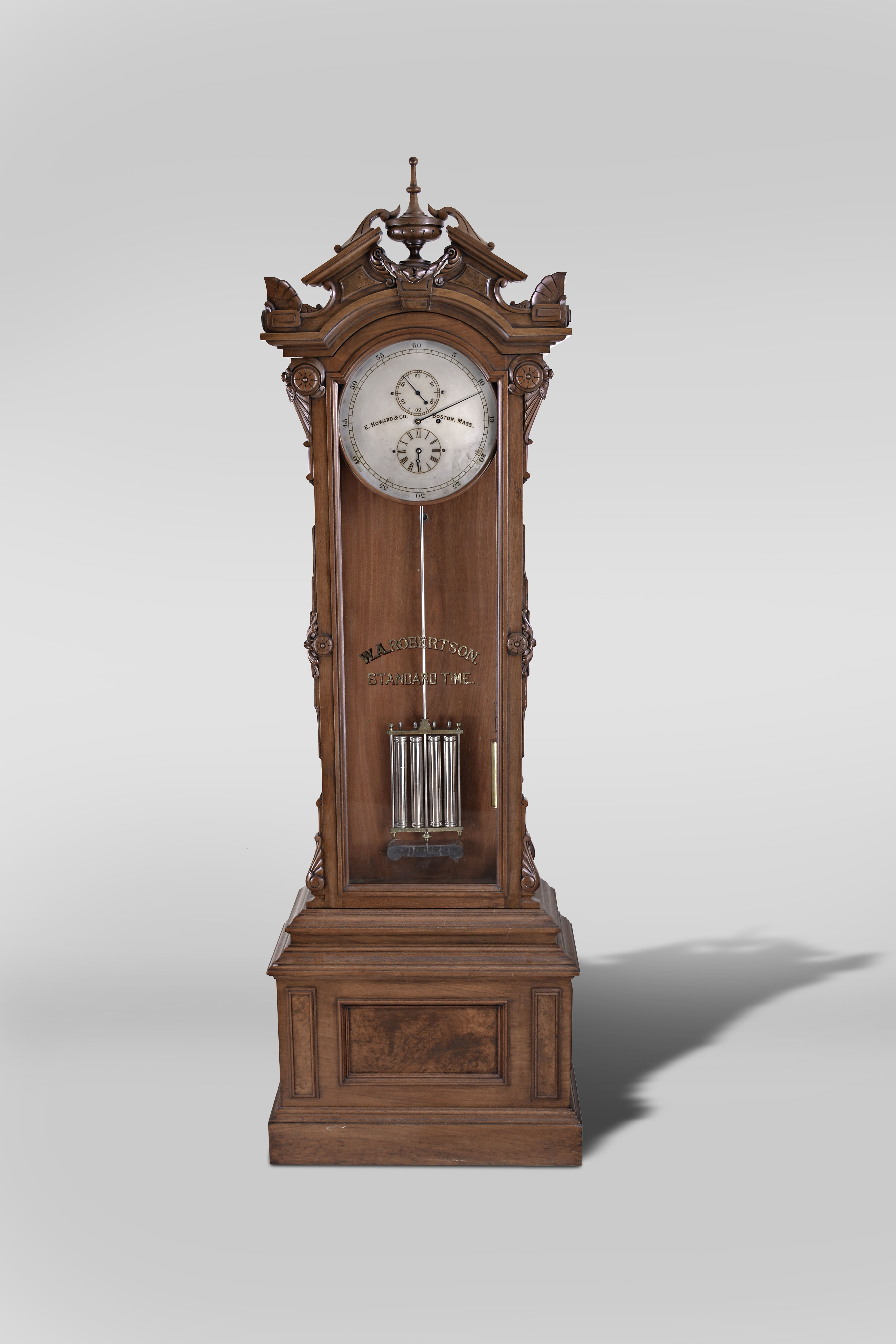 E. Howard &amp; Co., Boston, "No. 61" astronomical regulator, the renaissance revival style case with molded stepped base and burl veneered panels to the front and sides, and with cyma and cavetto molded top, supporting the upper case with glazed door and sides, the door with applied, stylized Grecian foliate carvings, and simple eight lobe roundels, arched cornice molding surmounted by a broken pitched pediment with central urn and laurel festoon, and the corners with stylized palmette form acroterion angularium above stylized, flattened volutes, door glass with reverse painted and gilded "W. A. Robertson Standard Time", silvered astrnomical dial signed "E. Howard &amp; Co. Boston, Mass.", blued steel hands, damascened brass week going movement with jewelled pallets, mercury pendulum with four nickel plated steel jars, brass frame, and nickel plated rod, silvered beat scale, brass clad weight, and heavy cast iron bracket attached to the case back, supporting both the pendulum and the movement — Antique Clocks Price Guide