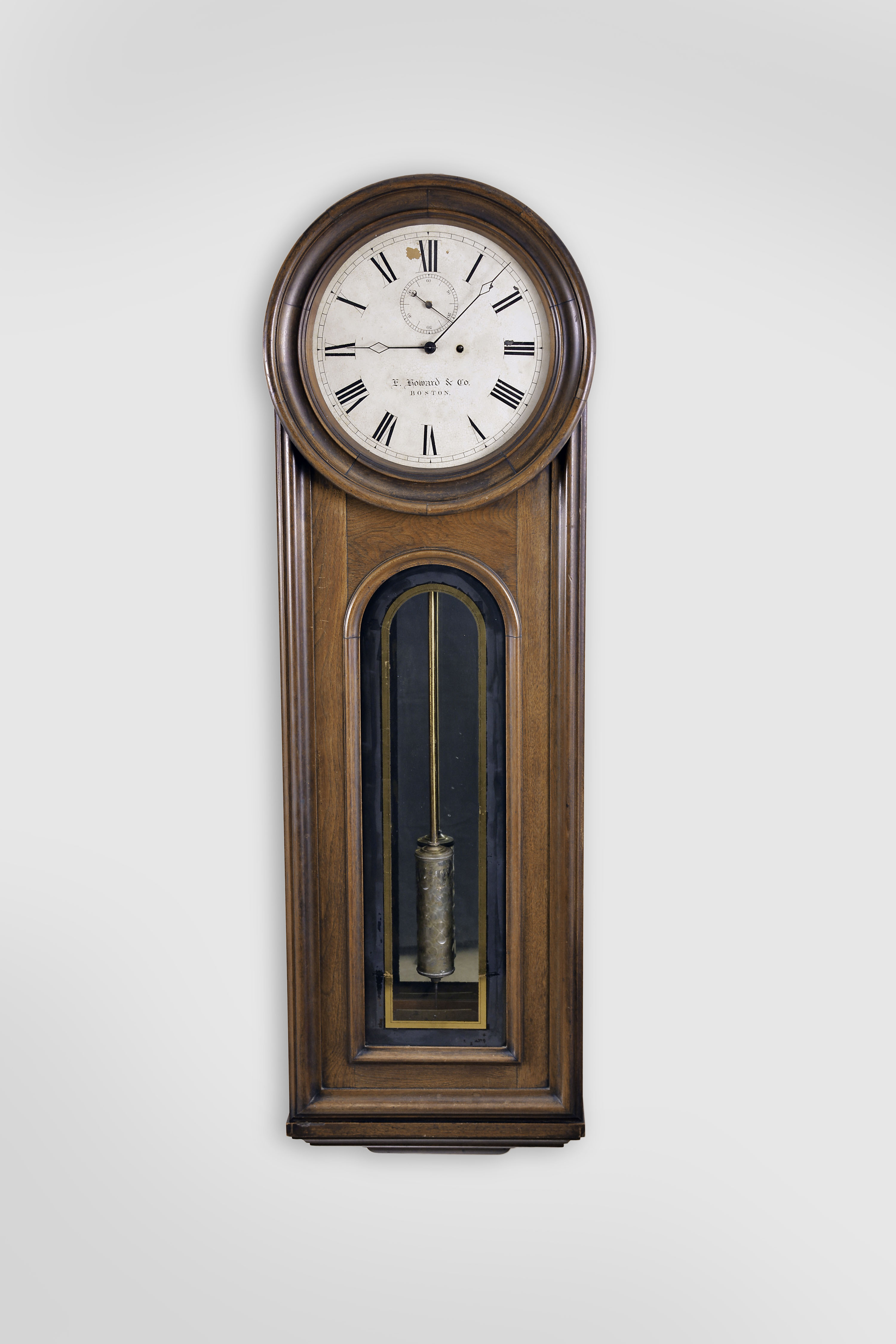 E. Howard &amp; Co., Boston, Mass., "No. 12 Regulator", wall clock, 8 day, time only, weight driven movement with a meter long compensated mercury pendulum with glass jar, in a walnut case with a painted metal dial and reverse painted tablet and on a purpose made special order base from the factory that allows the clock to stand on the floor. — Antique Clocks Price Guide