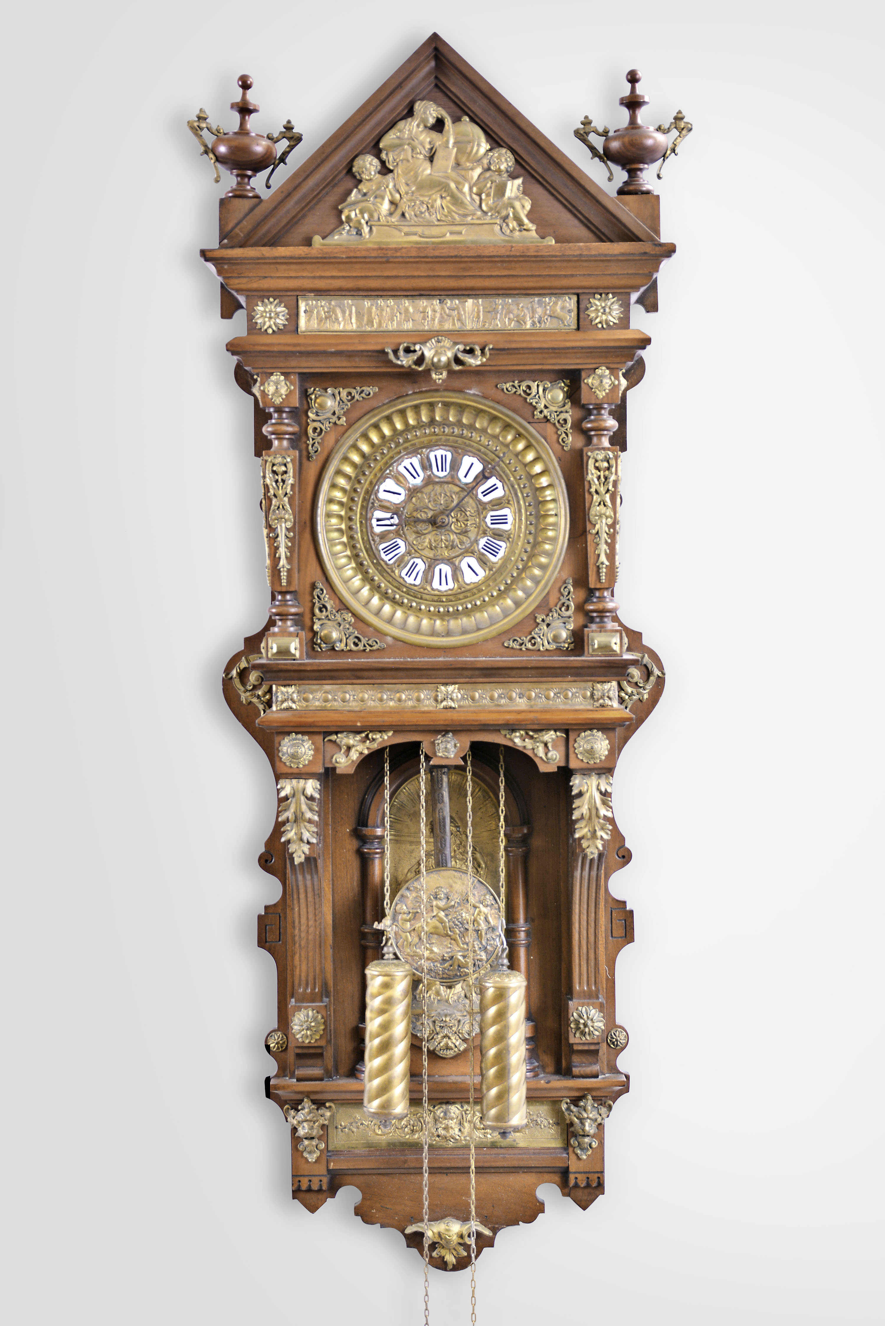 Ansonia Clock Co., New York, "Antique Hanging" wall clock, 8 day, time and strike, weight driven brass movement in a mahogany case with cast brass appliques, embossed pendulum bob and dial pan with turned weights — Antique Clocks Price Guide