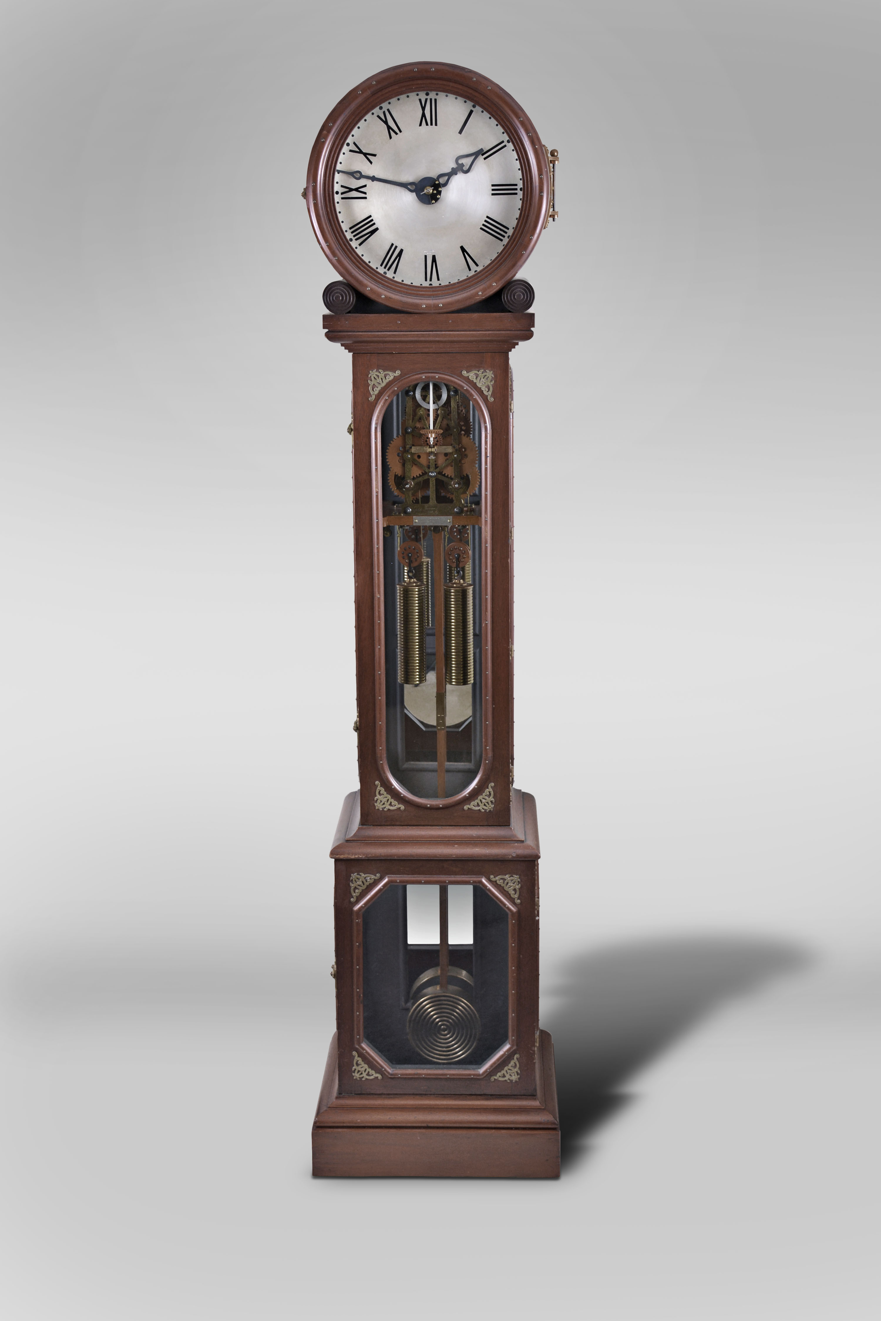 James Arthur, New York, an unusual drumhead regulator made as a wedding gift for his daughter, Bessie Humphrey Arthur, the mahogany case with glazed base and trunk, the glasses surrounded by half round moldings with decorative brass nails, and with applied, cast brass ornaments, decorative latches and hinges, the signed and dated timepiece movement with damascened, skeletonized brass plates and boxwood wheels, and visible through the trunk door, a bevel geared linkage extending into the drumhead top and driving the motion work, the seatboard with engraved presentation plaque, "Bessie Humphrey Arthur from her father James Arthur October 25th 1904", the movement driven by two reeded brass weights, with heavy brass disc pendulum decorated with turned, concentric beads, and the two piece wooden rod with beat adjustment device, all components reflected in the mirrored case back, silvered dial with pierced arabic numerals and minute markers, and blued steel hands of Arthur's design, together with a copy of Hering's "The Lure of the Clock", which documents the Arthur collection and his thoughts on clockmaking. — Antique Clocks Price Guide