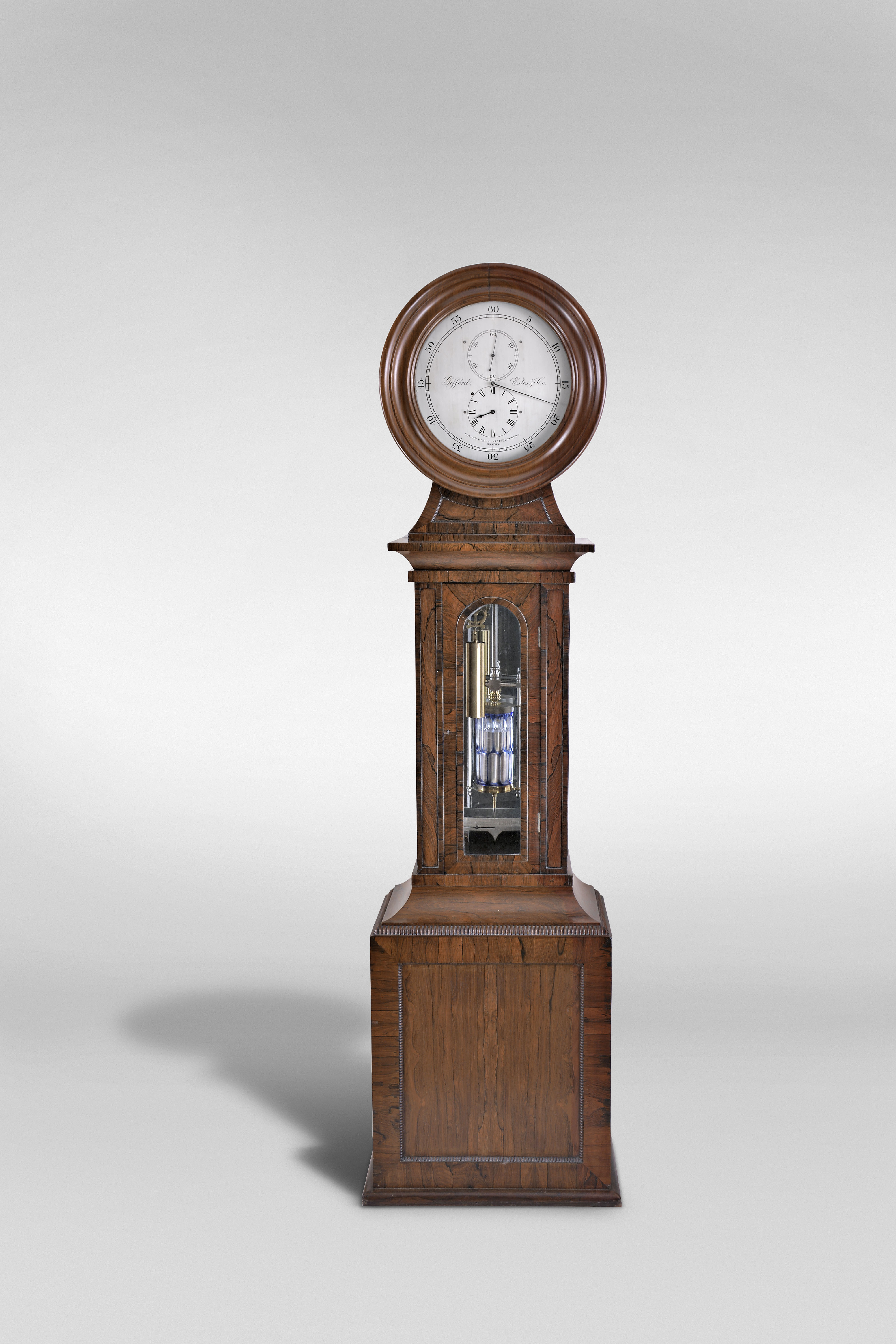 Howard &amp; Davis, Boston, Mass., a rare astronomical standing regulator, walnut, rosewood and rosewood veneer drumhead case, the base with turned, quarter round bead moldings framing recessed panels at the front and sides, and finished with a deep cavetto molding transitioning to the trunk, the trunk door with arched, crossbanded opening for viewing the weight and pendulum, and flanked by two narrow faux panels with crossbanded surround, the case sides also with glazed, arched windows, and surmounted by a cavetto molding below an incurved transition piece with conforming, molded panel, and supporting the drumhead with turned, molded door before the silvered brass dial, signed "Gifford, Estes &amp; Co.", and "Howard &amp; Davis Manufacturers, Boston", blued steel hands, large 8 day, weight driven timepiece movement with brass counterpoise for minute hand, jewelled pallets, pallet arbor, and escape wheel, and having adjustable steel endpieces throughout, brass weight with lyre form pulley, mercury pendulum with steel rod and decorative steel components, and blue cased glass jar with elongated, oblong clear cut panels, and with silvered beat scale, all before a mirrored case back, catching and reflecting light, and enhancing the decorative aspects of the various components — Antique Clocks Price Guide