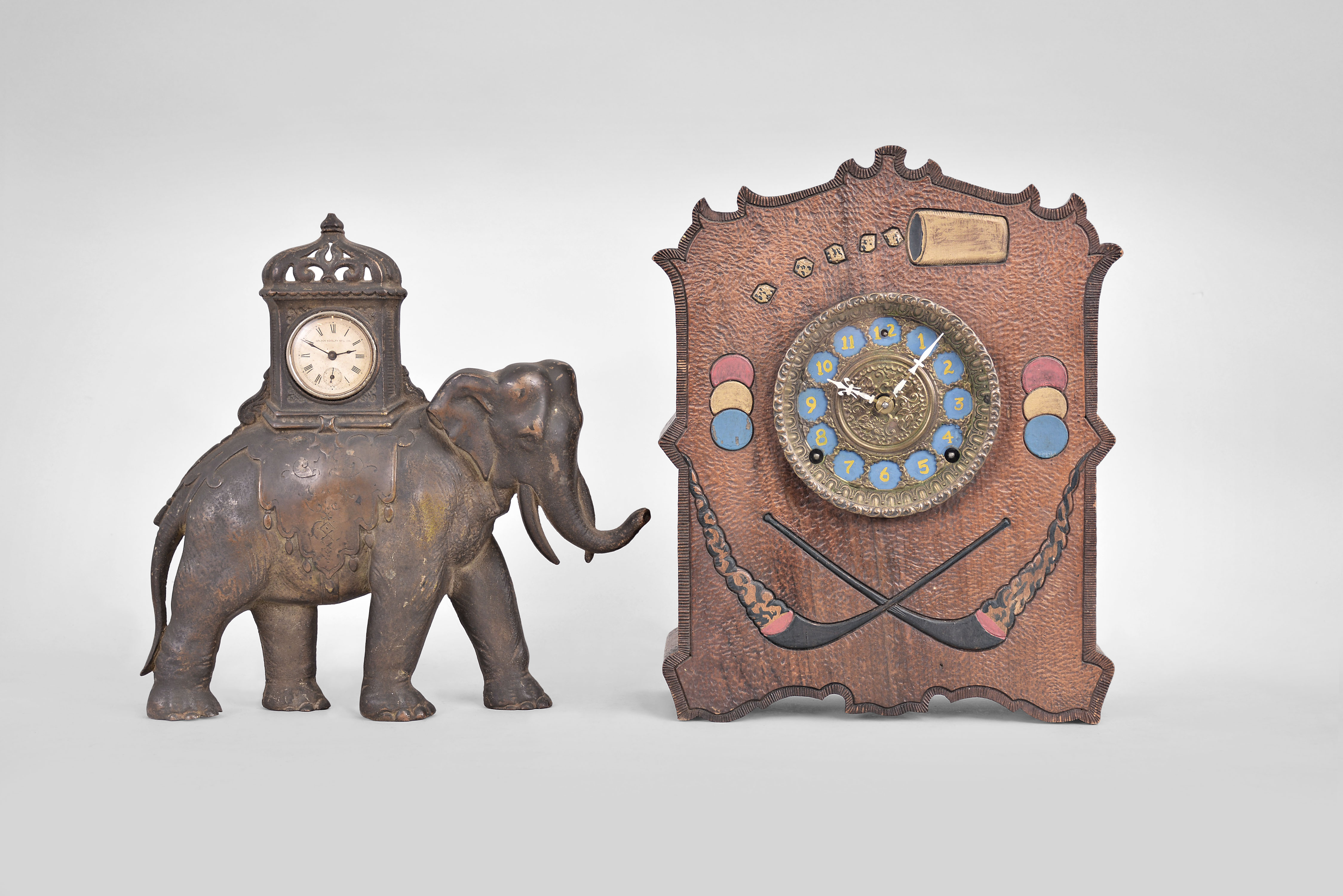 Clocks- 2 (Two): (1) Golden Novelty Mfg. Co., Chicago, elephant novelty clock, 30 hour, time only, spring driven balance wheel movement in a cast iron case shaped like an elephant, c1895; (2) Wm. L. Gilbert Clock Co., Winsted, Conn., "Cosey Corner, Pattern R" cabinet clock, 8 day, time and strike, spring driven movement in burnt wood case with dice, cards, poker chips, and domino designs, c1906. — Antique Clocks Price Guide