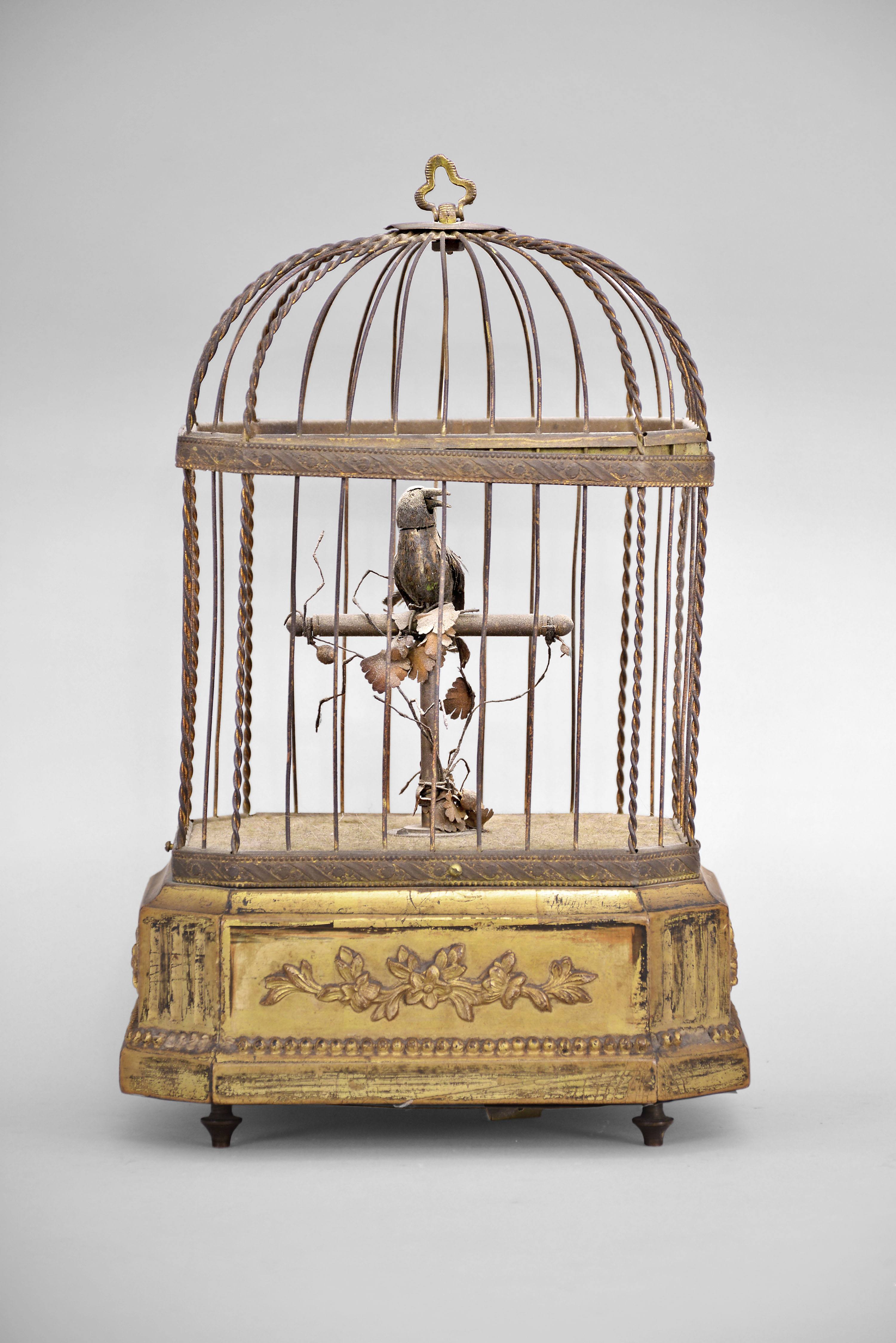 France, singing bird automaton, spring driven movement powers birdsong, as well as head, beak and tail feather motions, mounted on a gilt wood base with fluted canted corners and applied floral ornaments, the bird enclosed in a wire cage with velvet lined base and simulated flowers. — Antique Clocks Price Guide