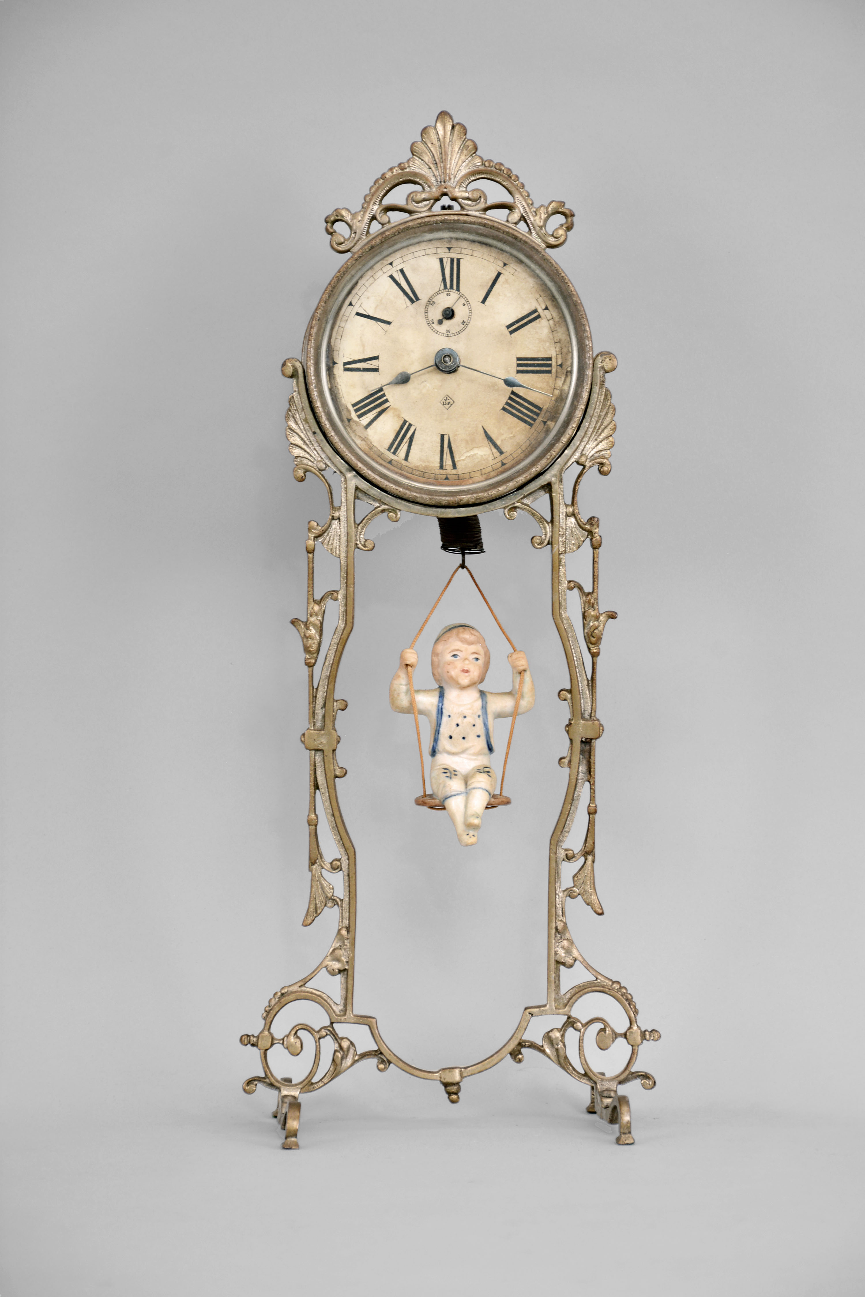 Ansonia Clock Co., New York, "Jumper No. 2" bobbing doll novelty timepiece, 30 hour, time only, spring driven movement that powers the clock and bouncing bisque doll, cast metal stand, 4 inch paper dial. — Antique Clocks Price Guide