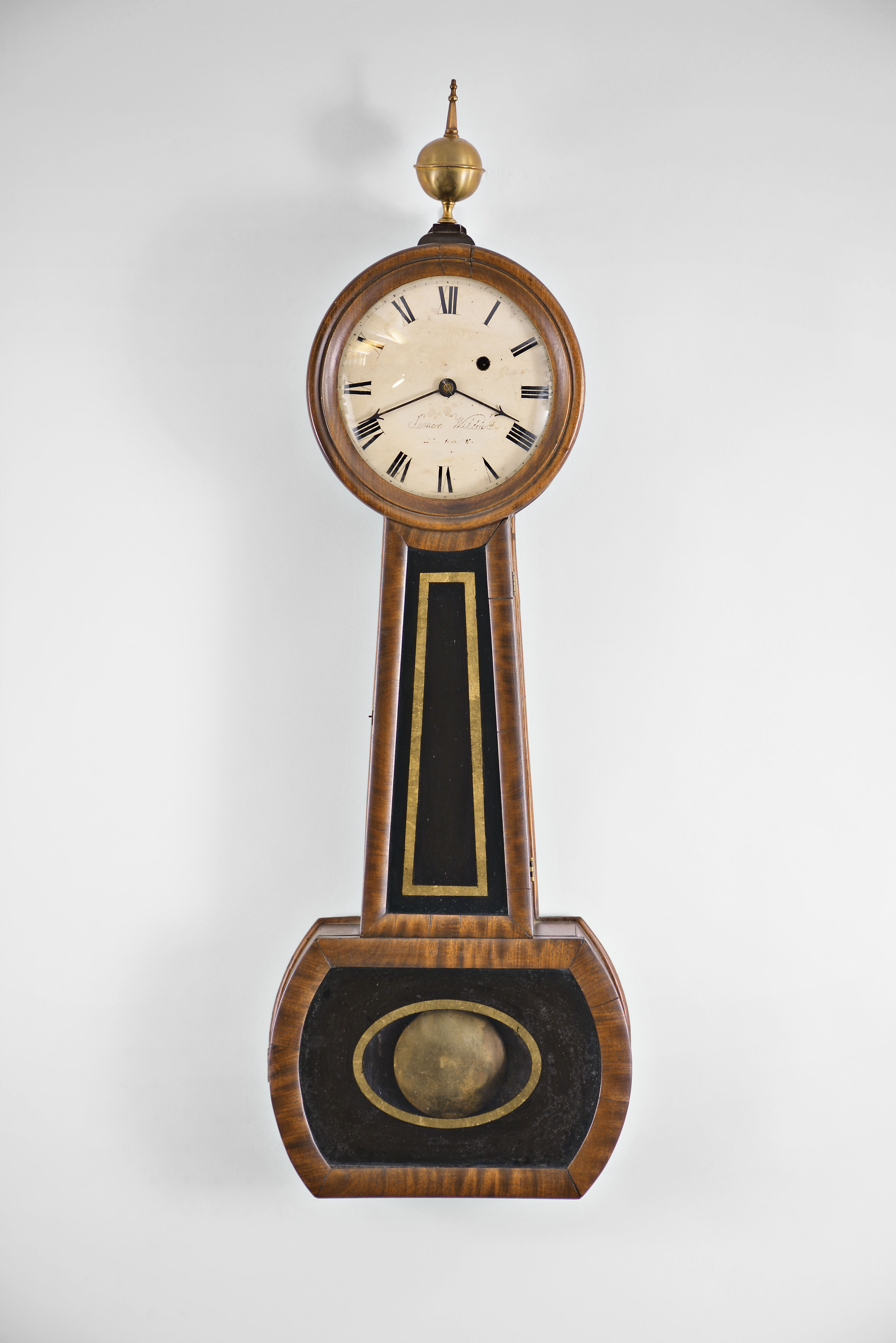 Massachusetts banjo wall clock, 8 day, time only, weight driven movement with T-bridge suspension in a mahogany and rosewood veneer case with hinged reverse painted throat and lower tablets and painted metal dial — Antique Clocks Price Guide