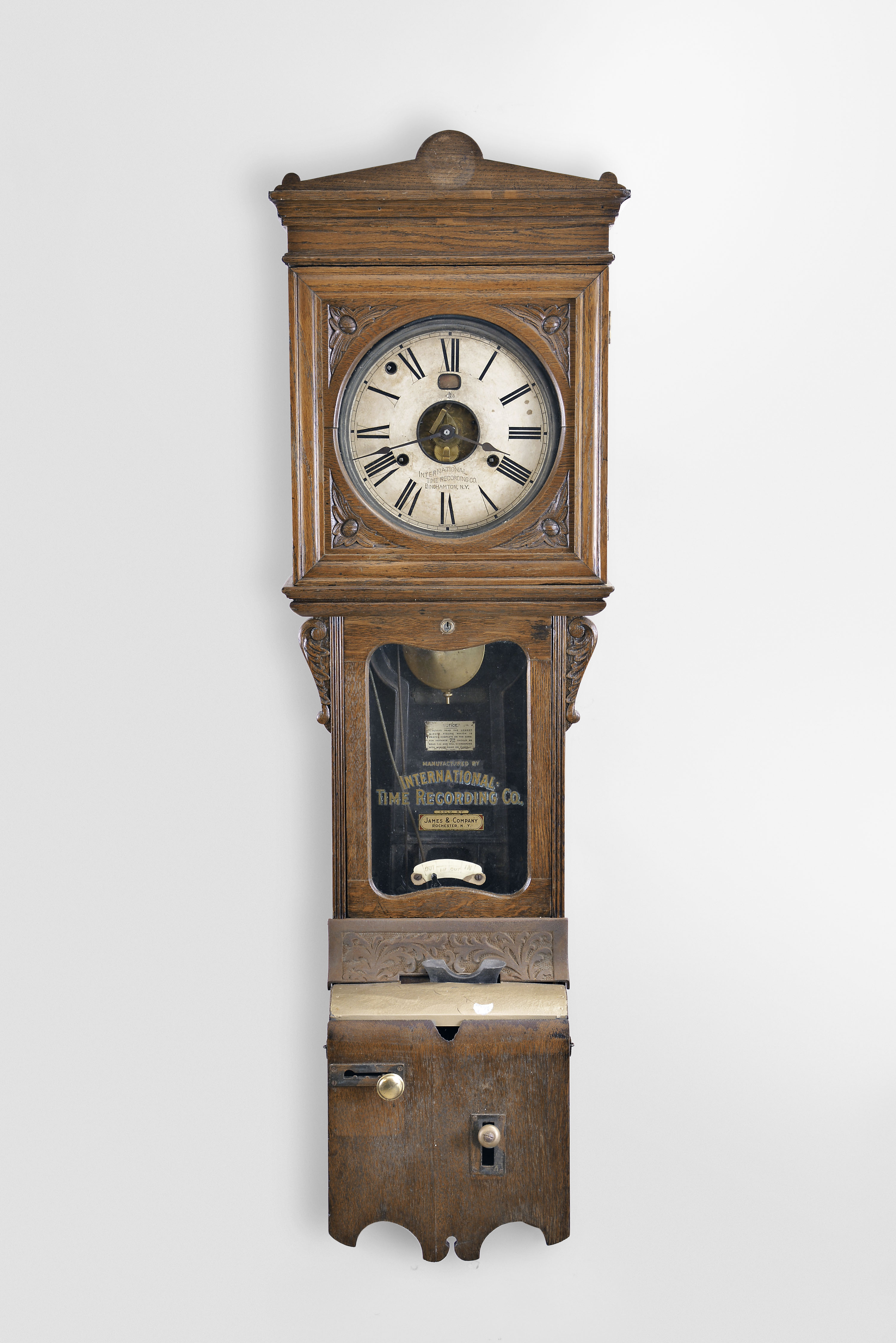 International Time Recording Co., Endicott, NY sold by James &amp; Co., Rochester N.Y., wall hanging punch clock, 8 day, time and day of the week, spring driven movement in an oak case with punch mechanism and painted metal dial with exposed center and day of the week aperture — Antique Clocks Price Guide