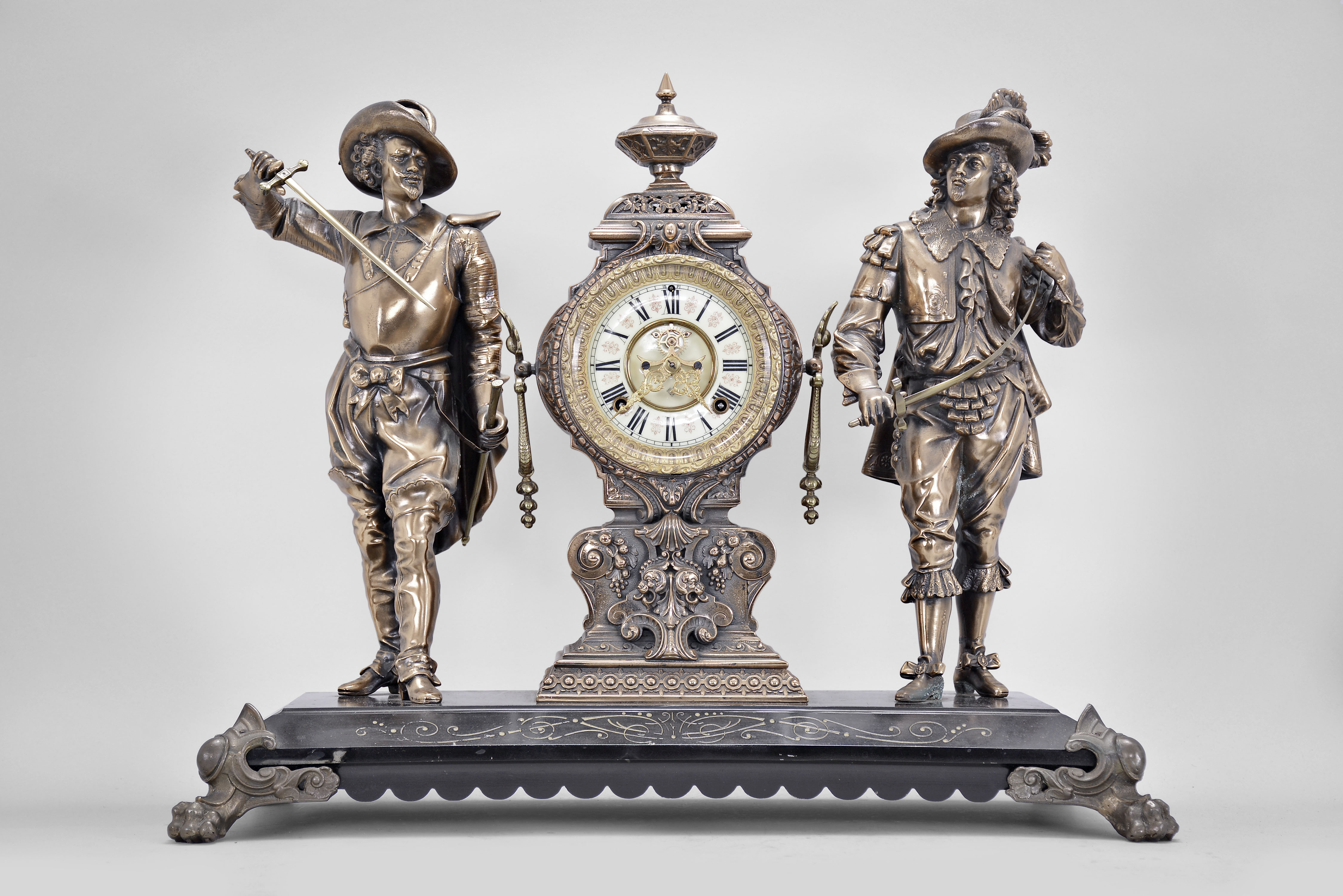 Ansonia Clock Co., New York, "Don Caesar and Don Juan" figural mantel clock, 8 day, time and strike, spring driven movement with visible Brocot escapement, black enameled iron base on paw feet supporting clock with cream enamel dial and Louis XV style hands, flanked by the two soldier figures. — Antique Clocks Price Guide