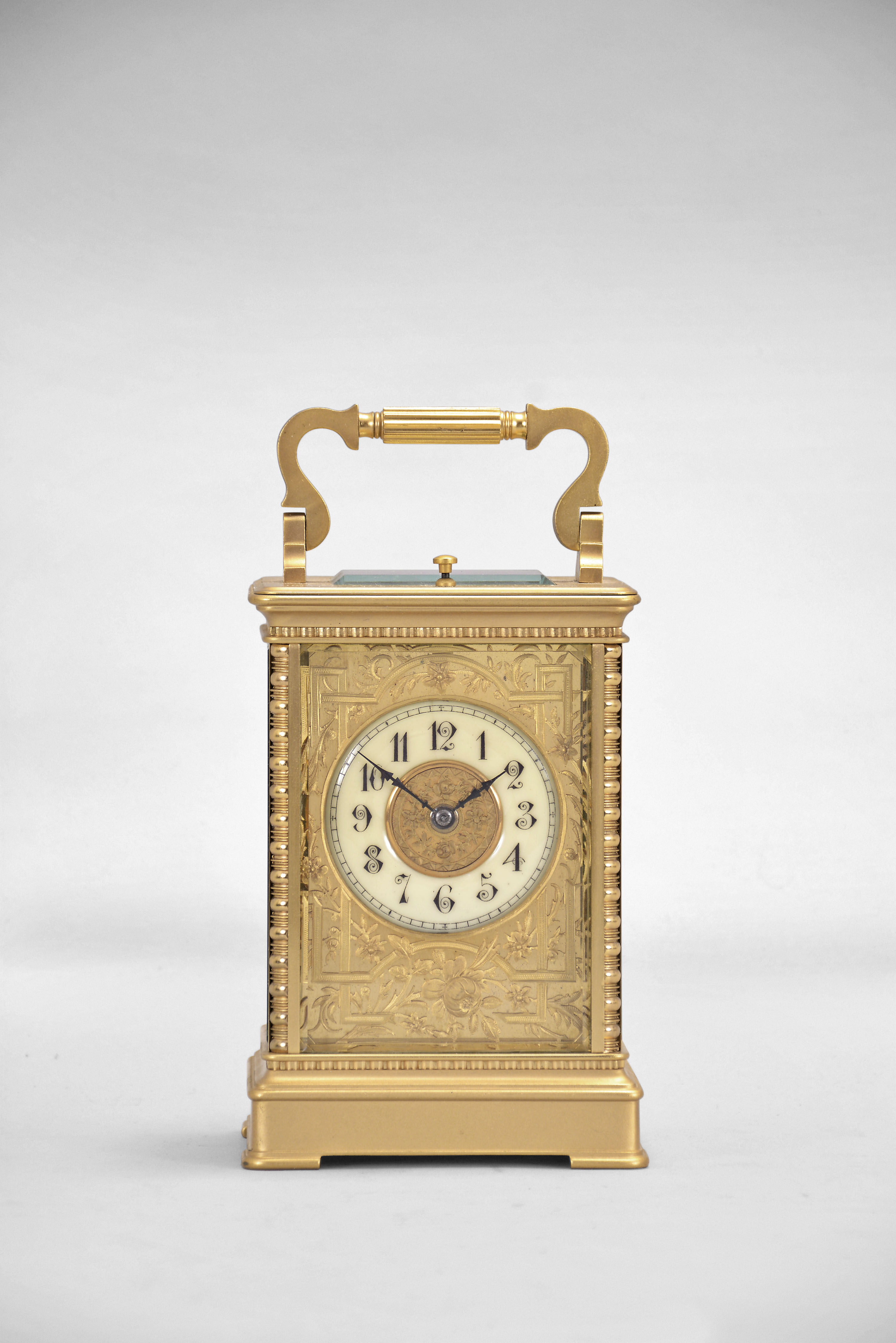 France, an unusual and decorative hour repeating carriage clock, the gilt, glazed, Anglaise Riche variant case with stepped base below a fluted band, the corners with bead and reel molding, and supporting an entablature echoing the base with simple molded cornice, the top with folding, Anglaise variant handle, Arabic numeral white enamel dial with blued steel distaff hands, the bright gilt mask with applied, finely chased, matte finished, gilt floral and foliate ornament, 8 day, two train movement with lever platform and cut bimetallic balance, striking the hour and half hour in passing, and repeating the last hour on demand — Antique Clocks Price Guide