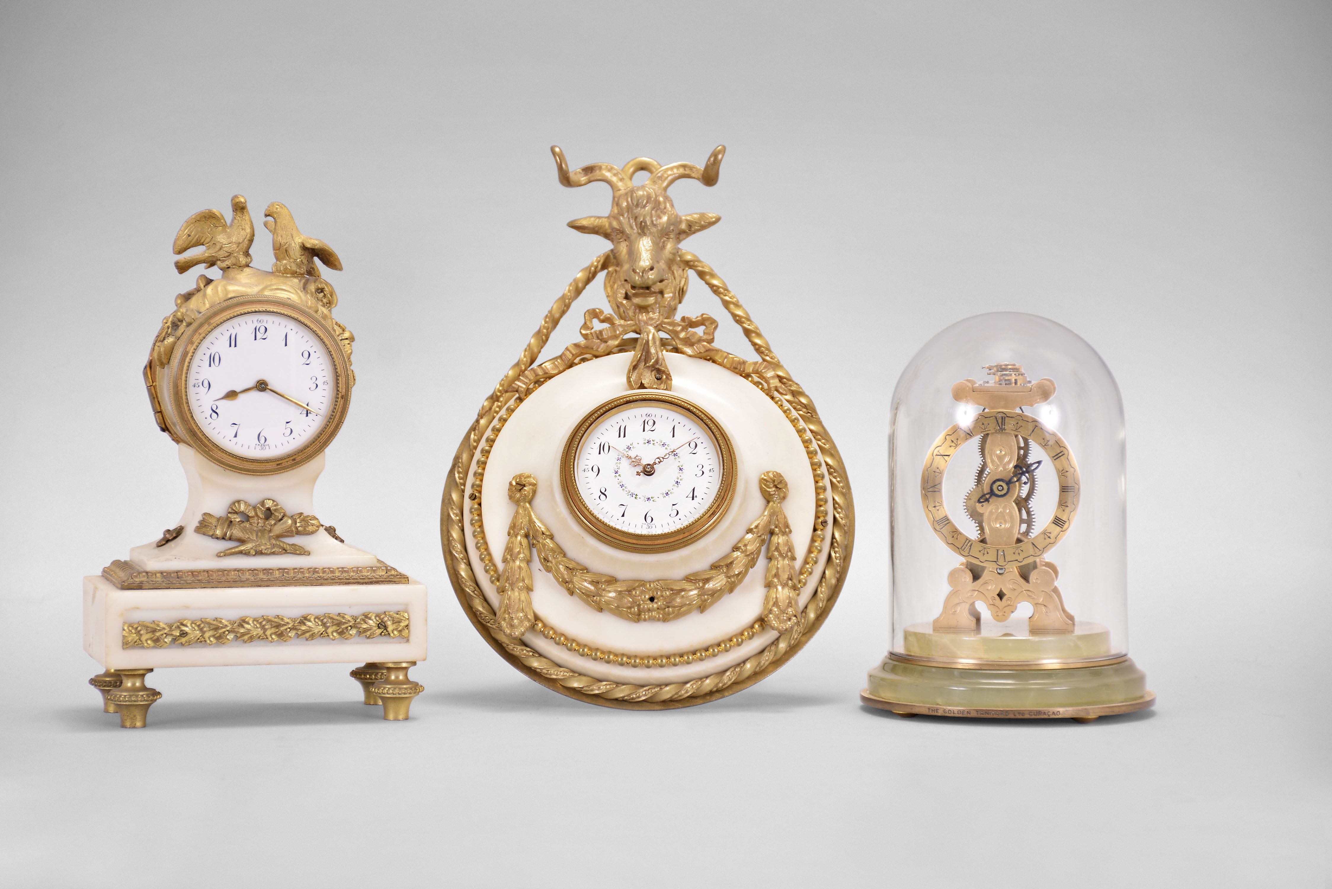 Clocks- 3 (Three) Charles Hour, Paris: (1) Miniature skeleton clock, 8 day, time only, spring driven movement with lever escapement on a green onyx base, under a small glass dome, c1910; (2) Desk clock, 8 day, time only, with jeweled balance wheel movement in a cast brass and white marble case surmounted by a pair of birds, c1900; (3) Desk clock, 8 day, time only, jeweled spring driven movement in a white marble case with applied metal ornaments and topped by goat's head, c1900. — Antique Clocks Price Guide
