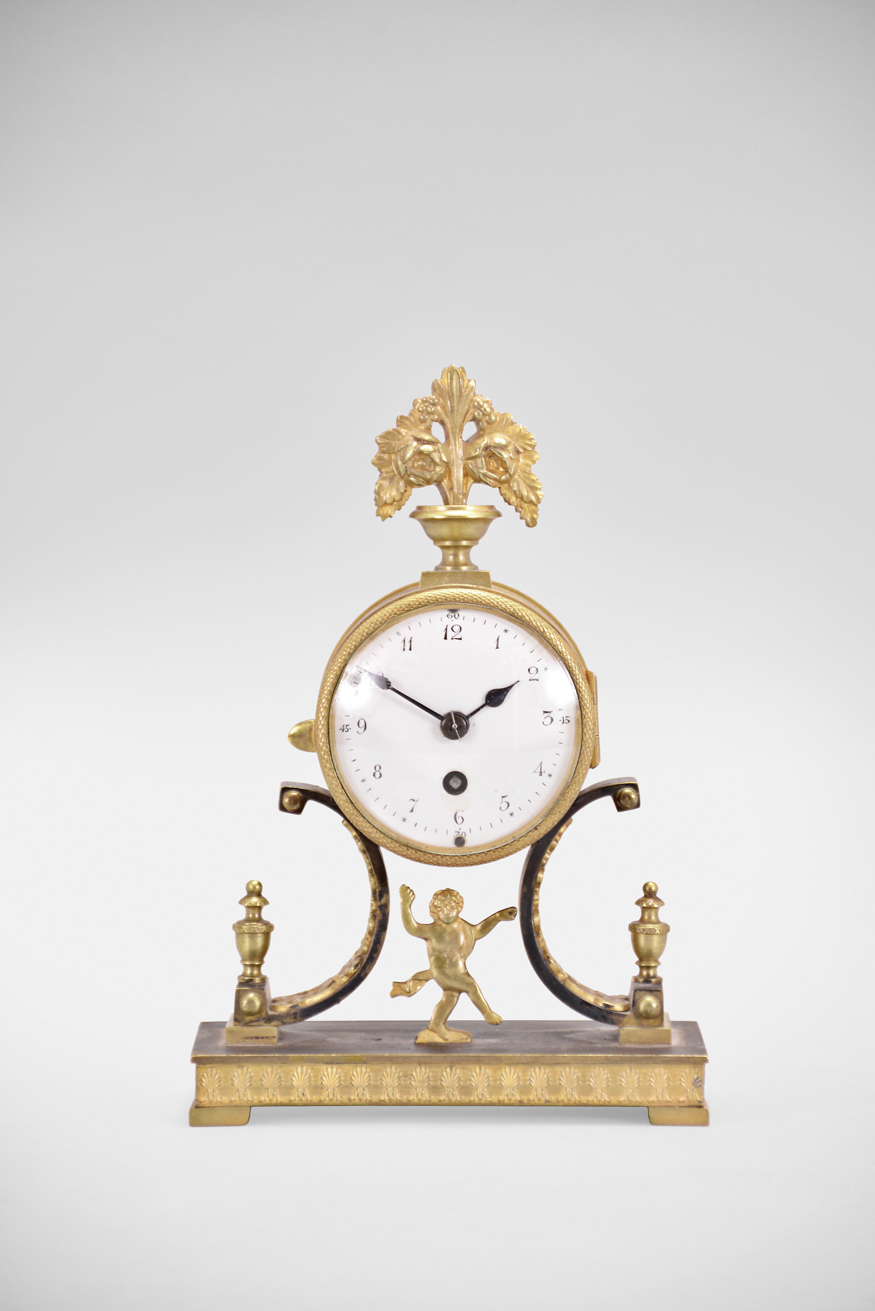 Lenzkirch AG, Lenzkirch, Germany, desk clock, 8 day, time only, spring driven movement with lever escapement in a cylindrical brass drum supported by an ornate cast brass case and topped with floral finial, white enamel dial with blued steel spade hands. — Antique Clocks Price Guide