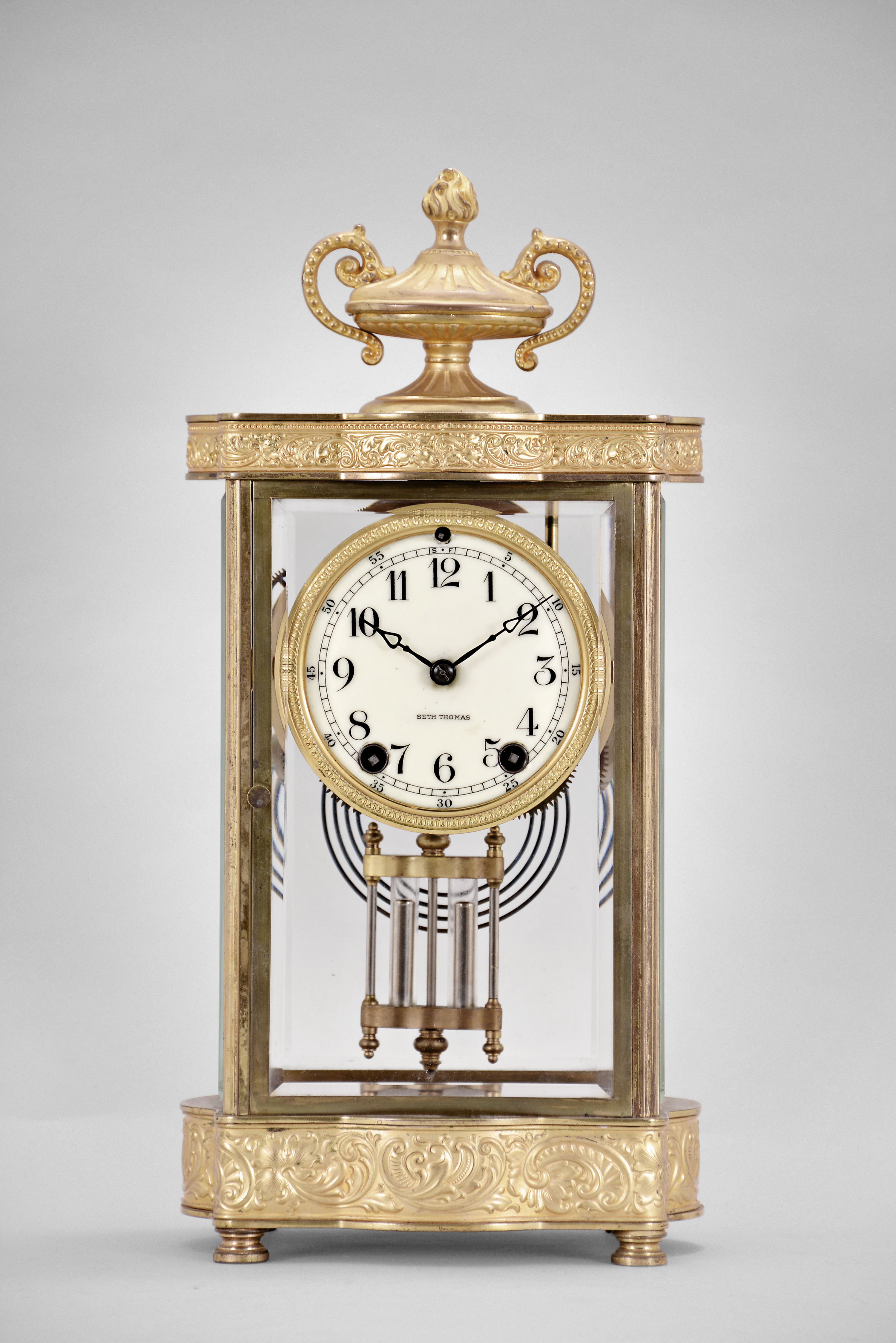 Seth Thomas Clock Co., Thomaston, Conn., "Empire No. 7" crystal regulator, 8 day, time and strike, spring driven movement in a glazed gilt brass case with urn finial, cream porcelain dial and blued steel hands. — Antique Clocks Price Guide