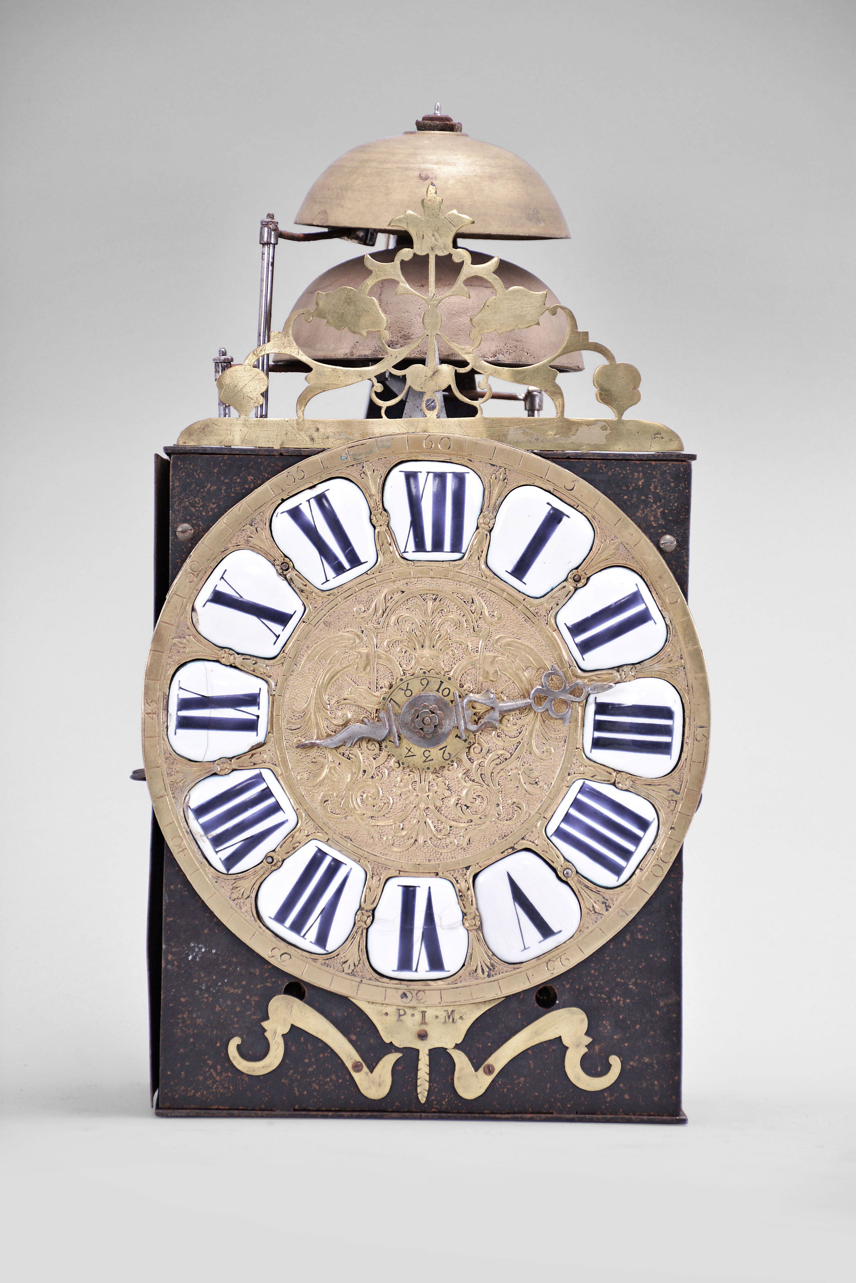 France, Comtoise clock, 8 day, time and strike with alarm, weight driven movement with verge escapement, thread suspension with rear-hanging pendulum in an iron post and plate frame, cast brass dial signed "P I M" with inset white enamel cartouches with blue Roman numerals, alarm ring with Arabic numerals, single iron hand, topped by a pierced brass fronton. — Antique Clocks Price Guide
