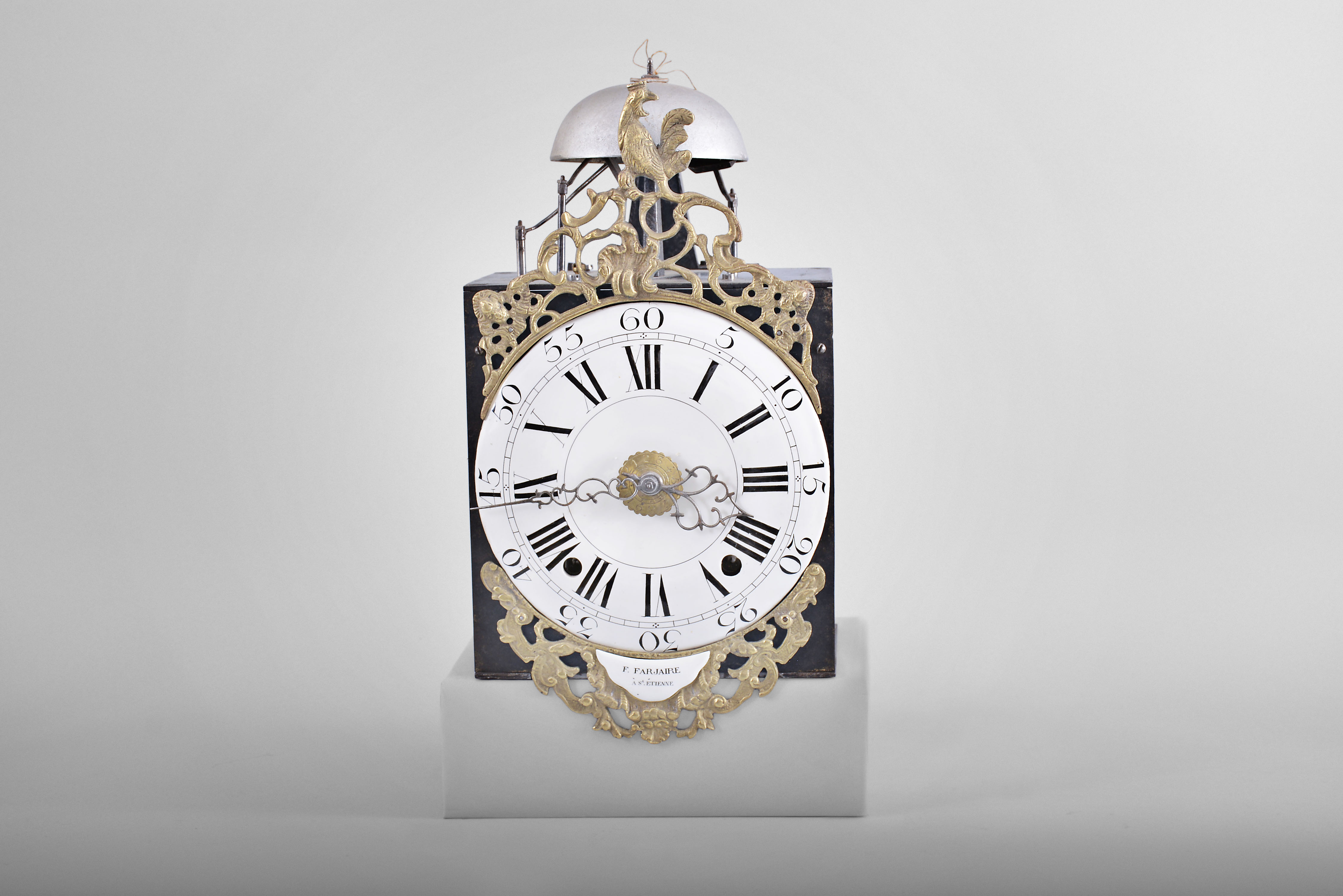 France, bronze-front Louis XV Comtoise clock, 8 day, time and strike with alarm, weight driven movement with alarm, verge escapement with thread suspension and rear-hanging pendulum in a posted frame, enamel dial with concave center and convex chapter, Roman numerals for the hours, large Arabic numerals at 5 minute intervals, brass alarm ring with Arabic numerals, two pierced iron hands, the clock is signed "F. Farjaire / A St. atienne" on an enamel panel below the dial, cast bronze fronton with the Gallic rooster. — Antique Clocks Price Guide