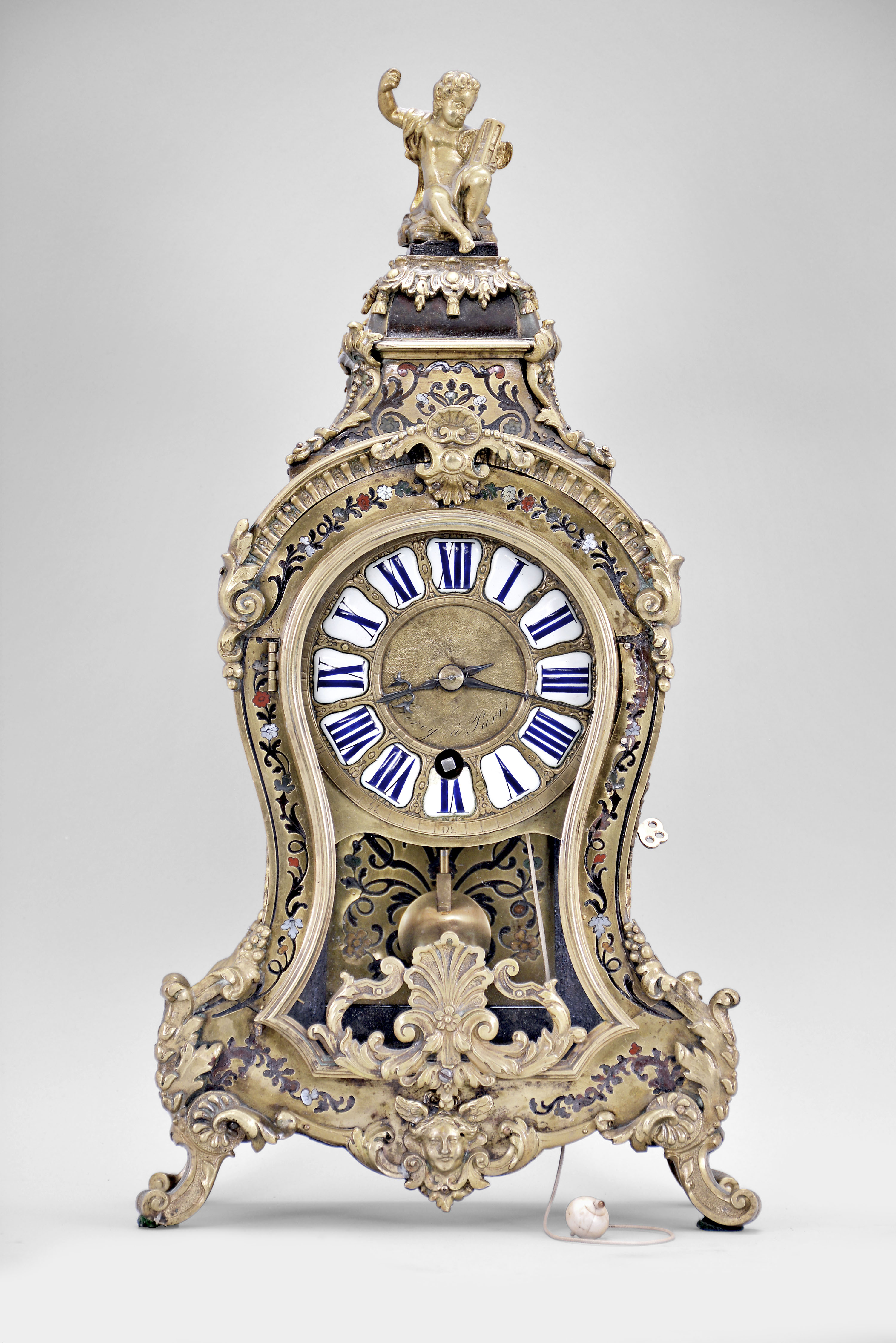 LeRoy, a Paris, a small Contre- Partie Boulle bracket clock with pull repeat, the case with polychrome, naturalistic ornament set into the brass veneer, the base with central mask, scroll feet, and foliate mounts conforming to the curves of the case, kidney shape, molded brass door with leaf and shell ornament, gadrooned brass cornice terminating in leaf and scroll mounts, and with central shell, the removable pagoda top surmounted by a seated figure of a small boy, in his left hand an hourglass with wings, and his right arm raised, the top concealing three bells, signed brass dial with Roman numeral enamel cartouches, finely finished blued steel hands, signed brass movement with tapered baluster form pillars, large barrel and five wheel train, crown wheel escapement, and sounding the last hour and quarter by pulling a cord, all resting on a matching, incurved bracket — Antique Clocks Price Guide