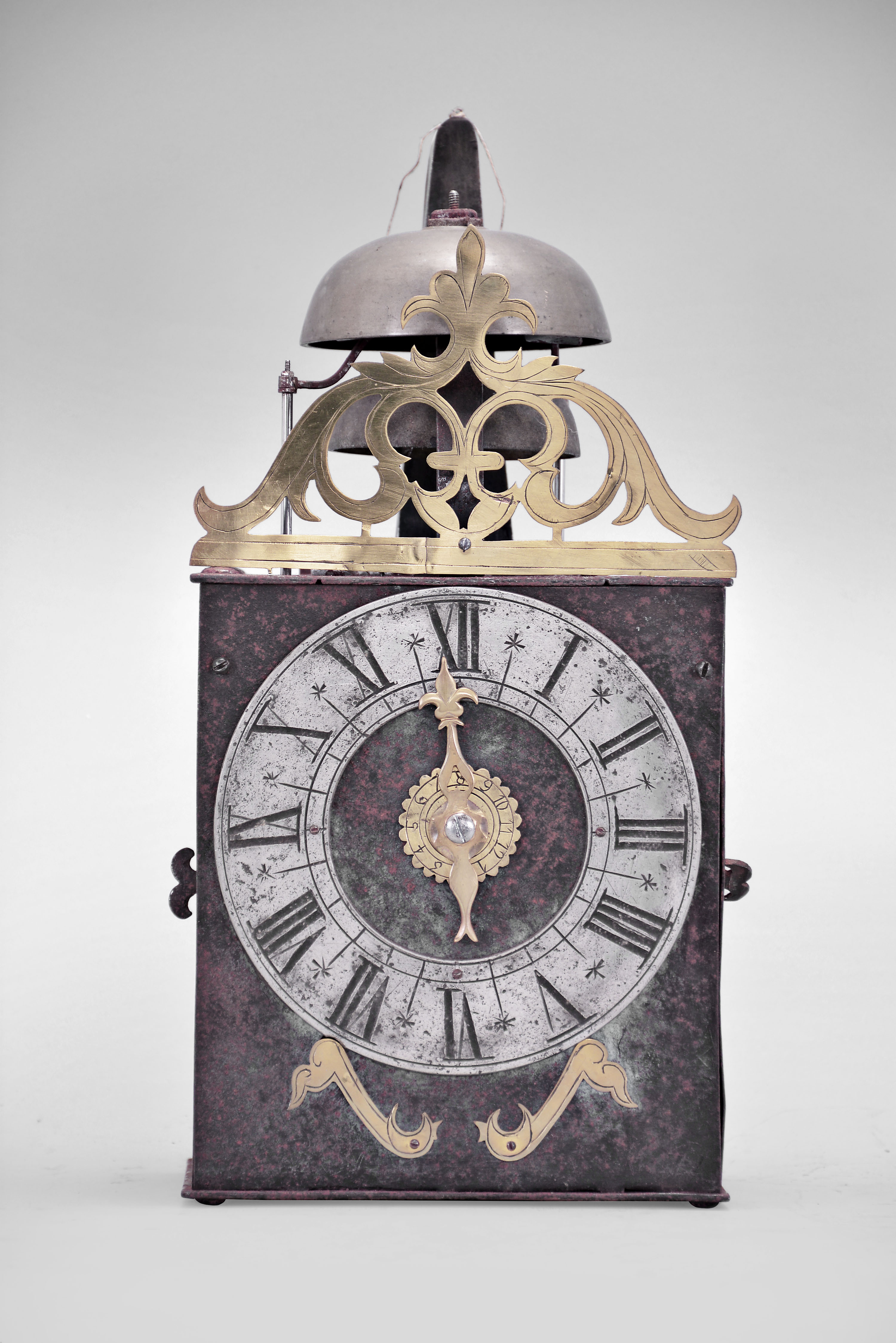 France, Comtoise clock, 8 day, time and strike with alarm, weight driven movement with verge escapement, thread suspension with rear-hanging pendulum in a iron post and plate frame, pewter chapter ring with engraved Roman numerals, brass alarm ring with Arabic numerals, pivoted brass winding arbor shutters with engraving, pierced brass fronton with engraving, and single brass fleur de lis hand. — Antique Clocks Price Guide