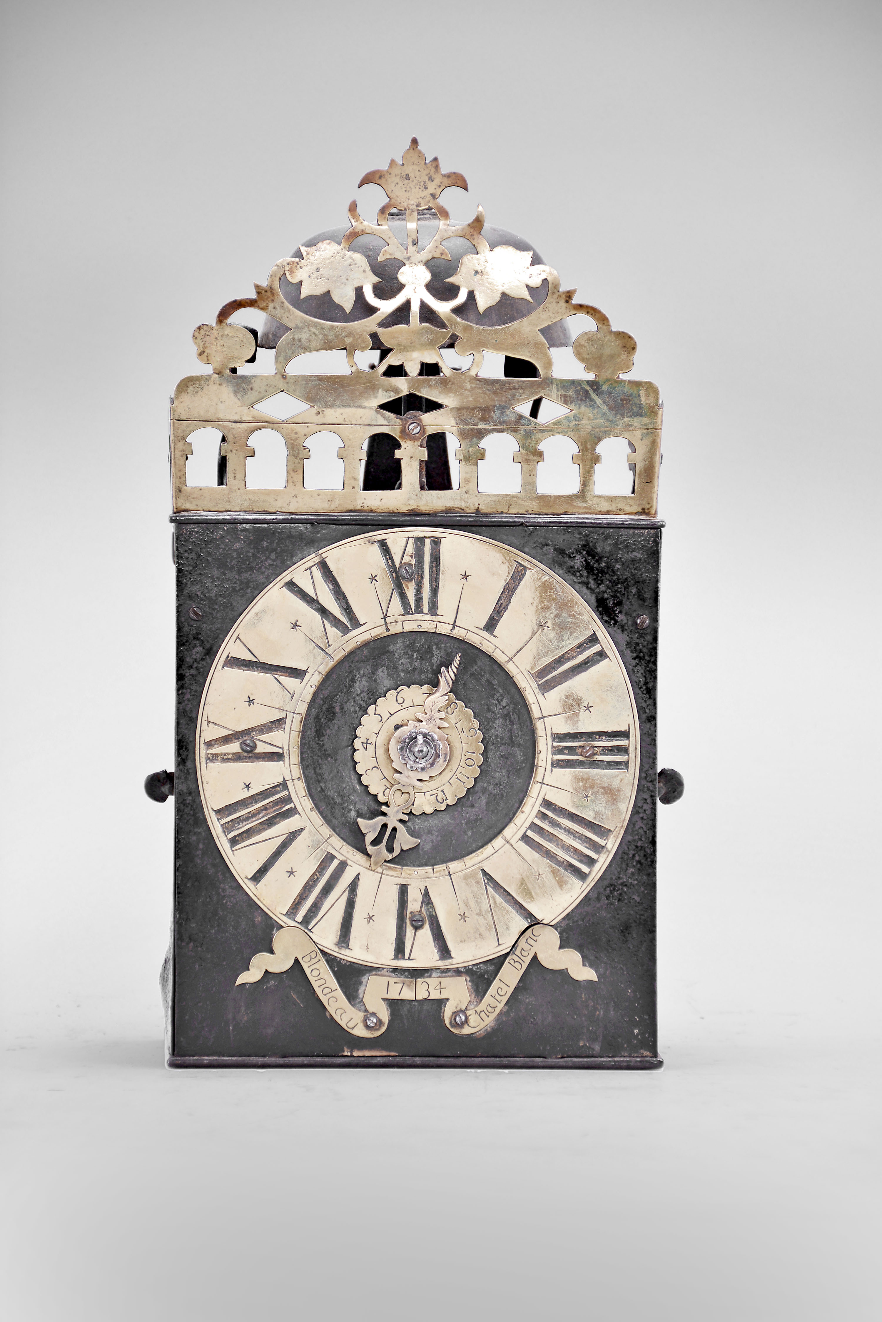 Blondeau, Chitelblanc, France, Comtoise clock, 8 day, time and strike, weight driven movement with Chevalier de Bethune escapement variant, thread suspension with rear-hanging pendulum in a iron post and plate frame, brass chapter ring with engraved Roman numerals, brass alarm ring with Arabic numerals, pivoted winding arbor shutters engraved with "Blondeau / 1734 / Chatel Blanc", single pierced brass hand, the top sides and front with one piece arcaded gallery with integrated pierced and engraved brass fronton. — Antique Clocks Price Guide