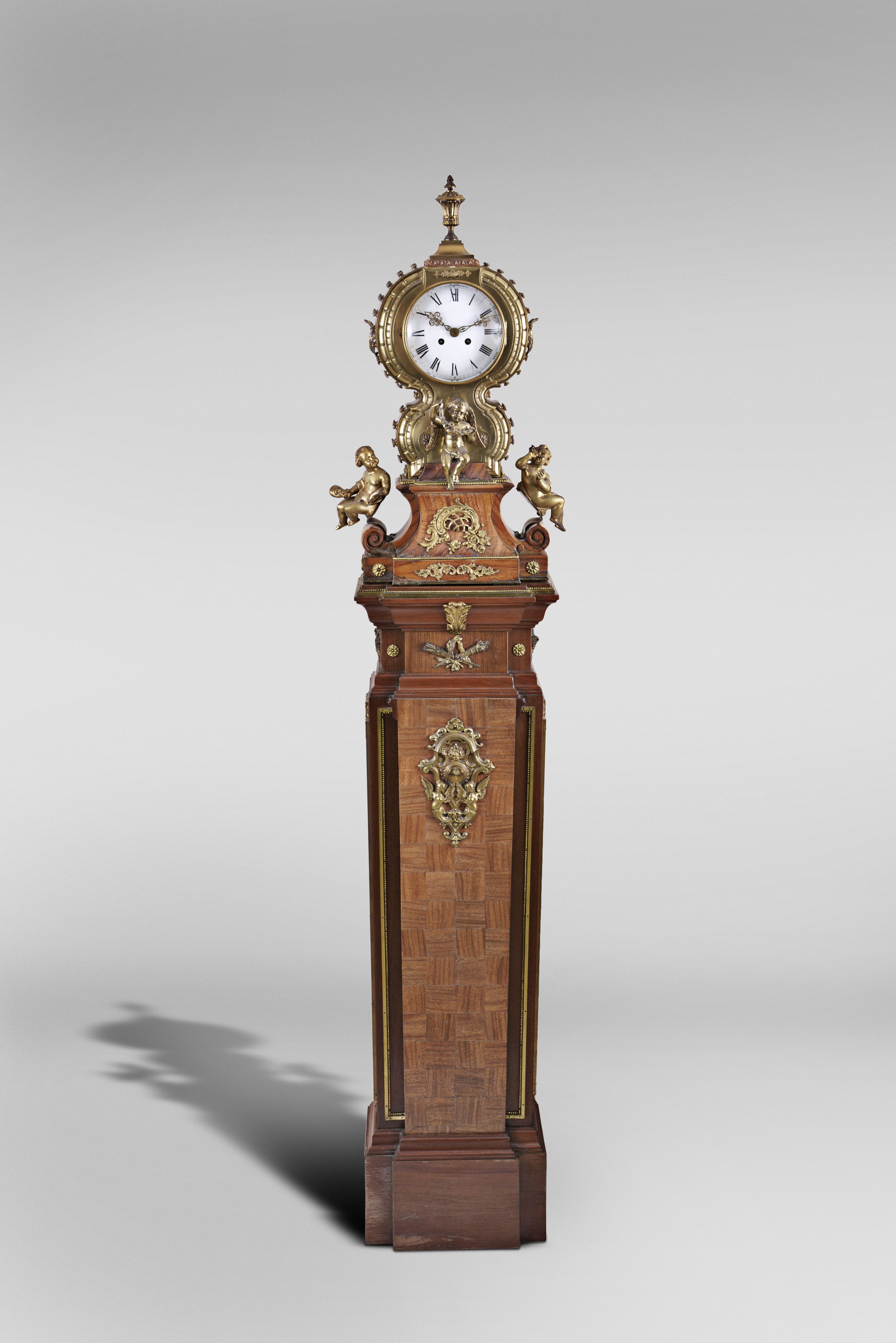 Marti &amp; Cie, Paris, France, figural shelf clock, 8 day, time and strike, spring driven movement with white enamel dial in a highly stylized cast brass case set on veneered wooden base surmounted by three putti grasping bacchanal themed items and cast brass appliques including matching stand with cast brass appliques, veneers and ornaments. — Antique Clocks Price Guide