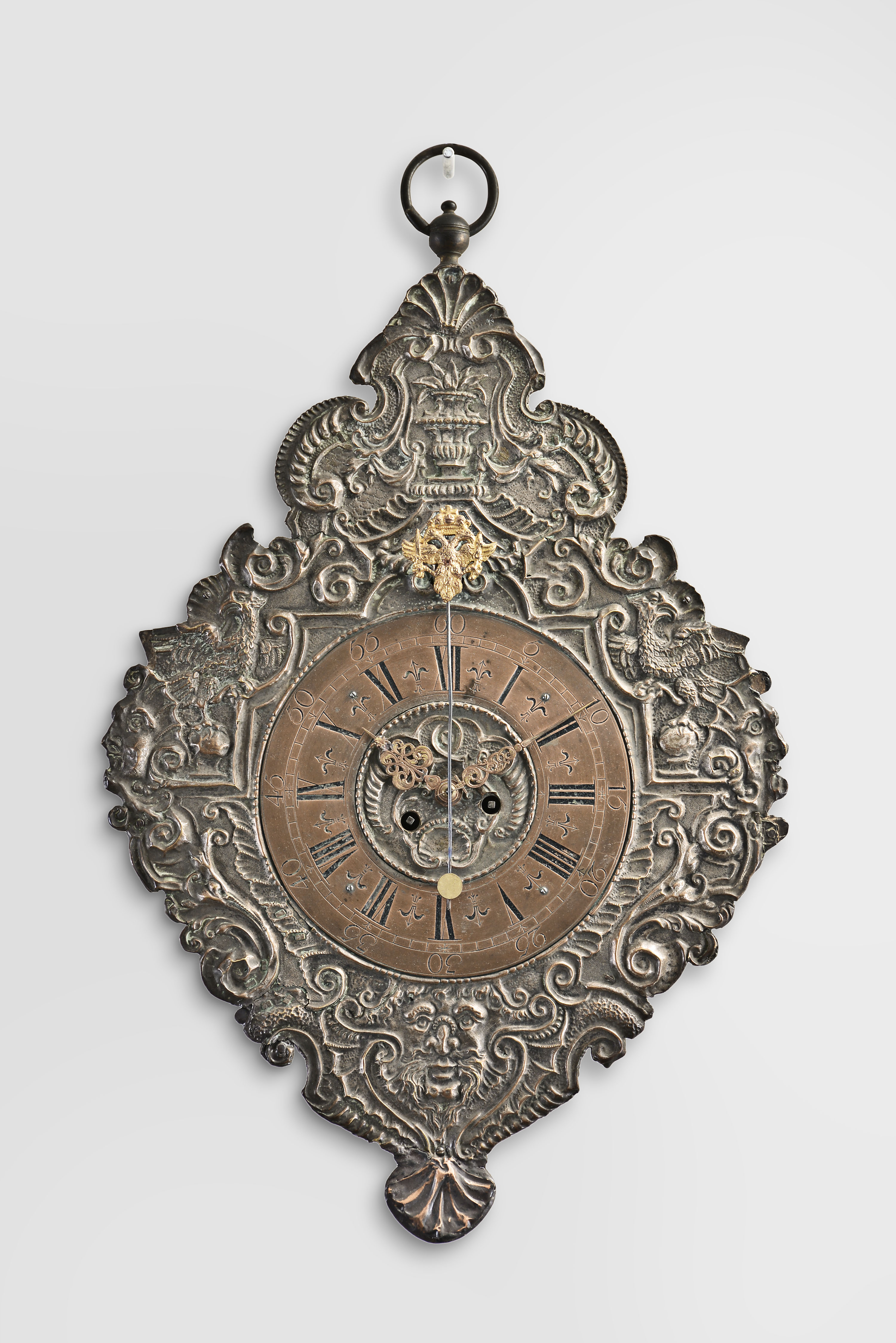 Southern Germany or Austria, telleruhr clock, 8 day, time and strike, spring driven movement with verge escapement and cowtail pendulum, mounted to an iron plate covered in copper relief birds, palmettes, and human faces on a scrolling field, the pendulum arbor cover in the form of a double-headed eagle, copper chapter ring with Roman numerals for the hours and Arabic numerals at five minute intervals, pierced brass hands with copper finish. — Antique Clocks Price Guide