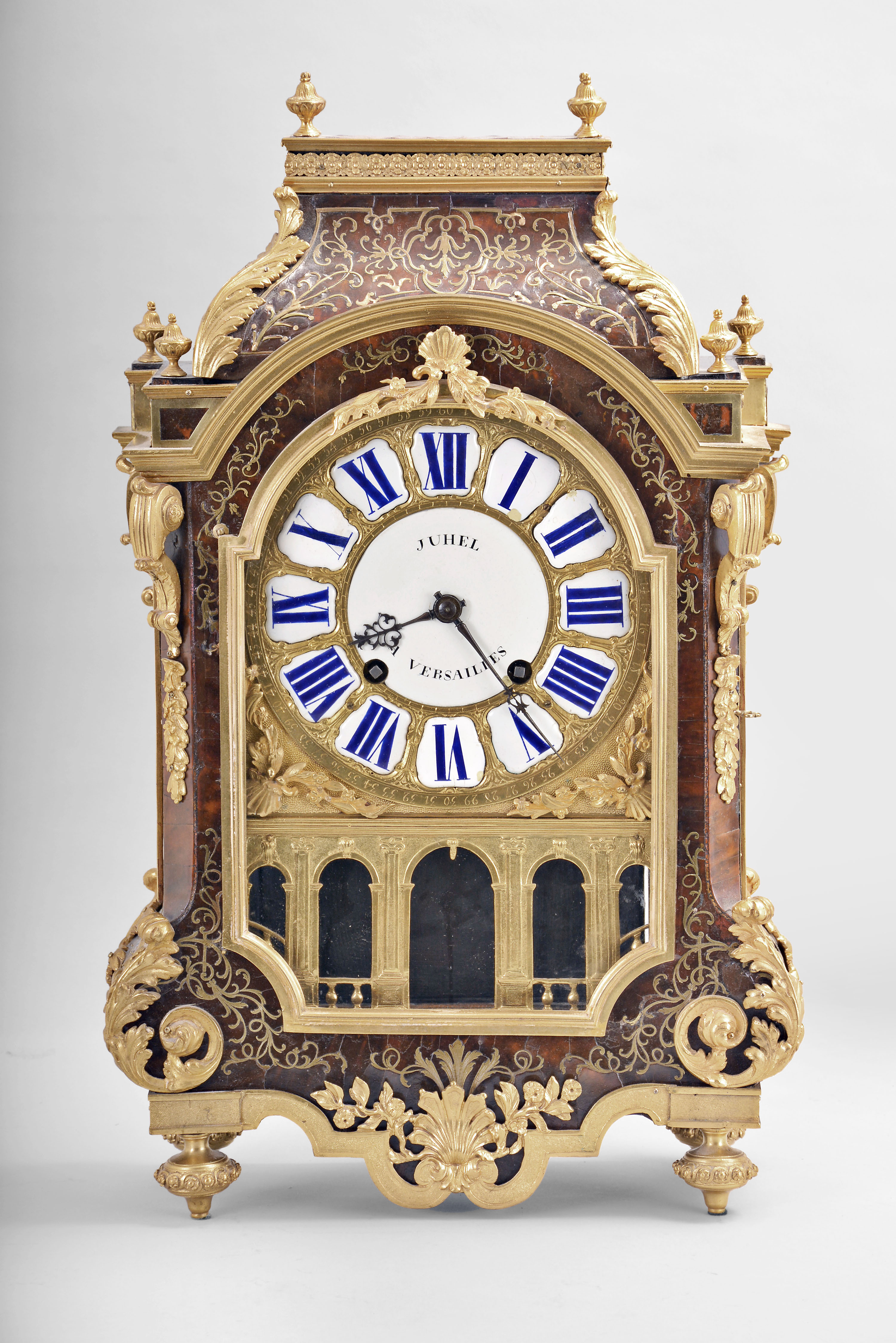 Ourry, a Paris, a large Boulle work and ormolu mounted bracket clock, the case on four turned and flower ringed feet, undulating skirt with conforming bronze mount having a central shell and foliage, arched door with incurved lower corners, and flanked by scroll brackets, foliate drops, and acanthus scrolls, arched cornice molding below a step with corner finials, and surmounted by a removable, cyma curved top, with acanthus corners, floral frieze, and four more urn finials, roman numeral enamel cartouche dial with gilt surround, the enamel center signed "Juhel a Versailles", numbered disc above 12:00 for regulation, and nicely made blued steel pierced and filed hands, above a gilt, architecturally detailed arcaded fret, the rectangular brass movement of at least two week duration with five baluster form pillars, with crown wheel escapement, silk thread suspension, cycloidal cheeks, and count wheel striking, the back plate signed "Ourry a Paris", with large iron key, three partial pendulums, and a 20th century bracket — Antique Clocks Price Guide