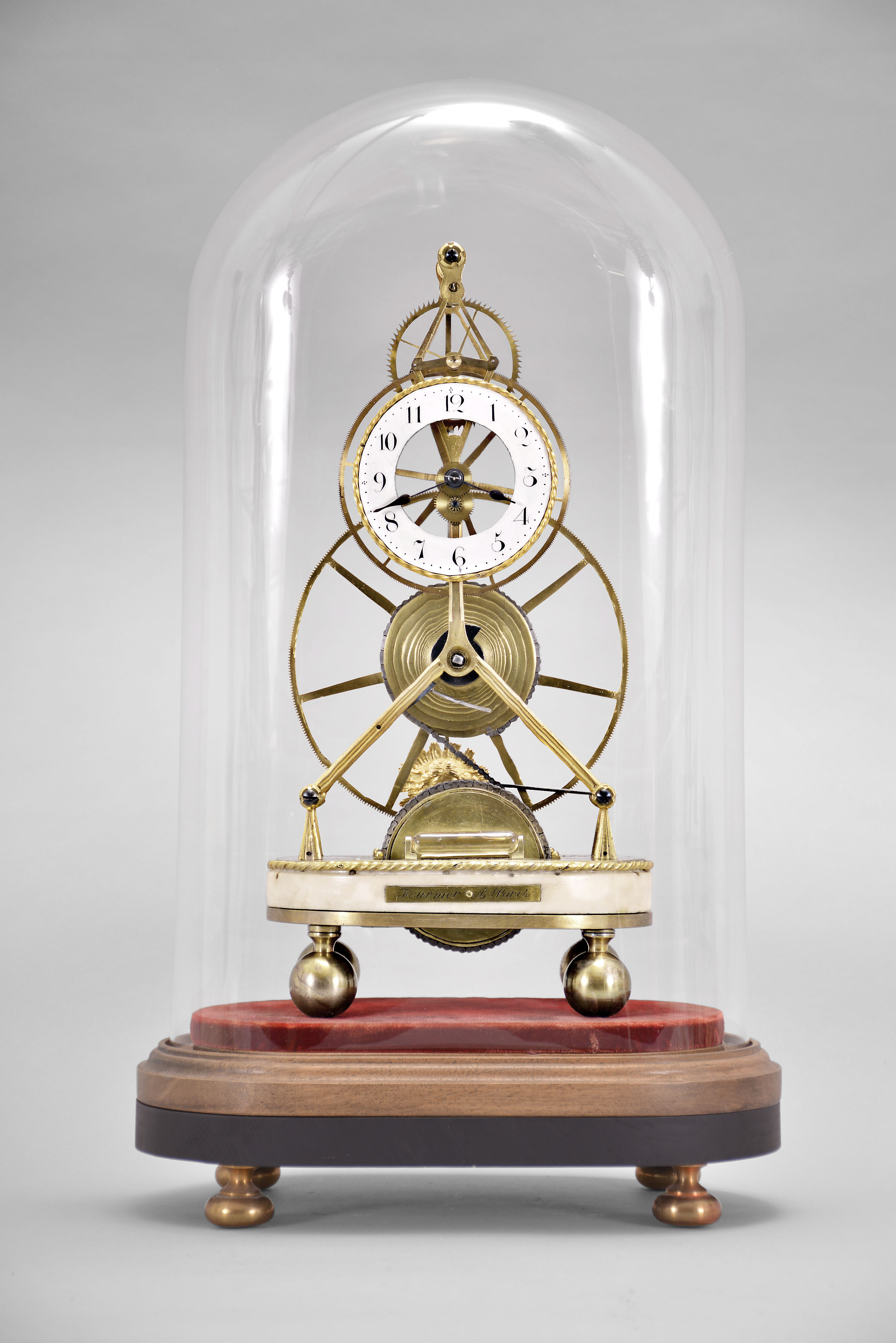 Fournier, a Paris, an early 19th century, month going great wheel skeleton clock, the gilt, inverted Y frames joined by three cylindrical pillars with molded and knurled ends, 6 1/2 inch great wheel with fusee, driven by a large barrel partially concealed in the white marble base, the second wheel concentric with and slightly larger than the Arabic numeral white enamel dial, tic tac escapement with silk thread suspension, blued steel spade hands, and gilt Medusa mask pendulum, the whole resting on ball feet, and under an oval dome with conforming wooden base — Antique Clocks Price Guide