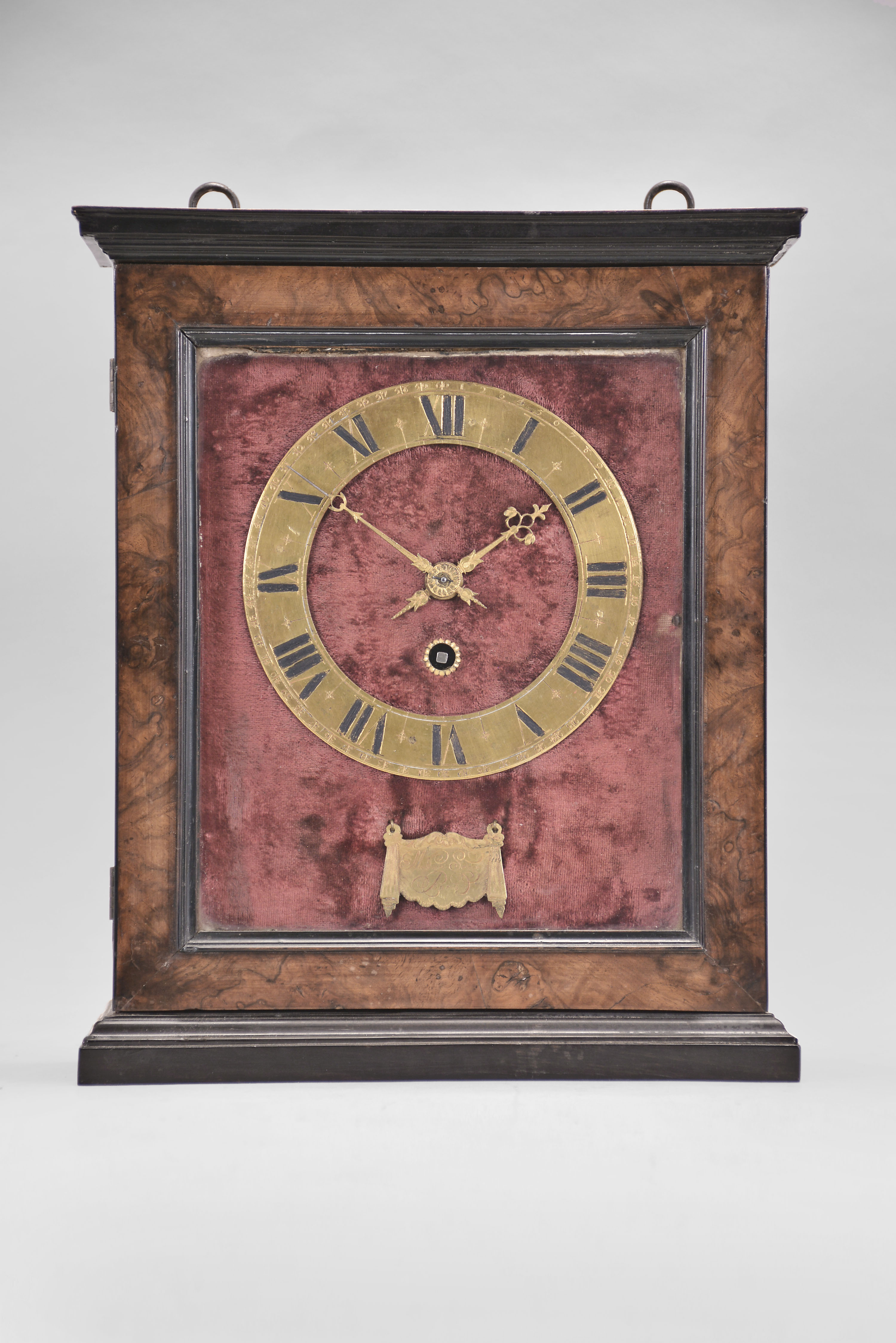 Mathurin Souge, a Paris, a 17th century French "Hague Clock", the oak and walnut case with burl walnut veneer, the top, base and door with ebonized moldings, the sides having arched windows with ebonized surrounds, and top with two iron loops for hanging, interior of the case back with figured walnut veneers bordered by plain walnut with ebonized string inlay, red velvet lined brass plate with gilt dial and fancy pierced and engraved gilt hands, the minute hand with steel tip, hinged, engraved lambrequin below 6:00, signed "Mathurin Souge, A Paris", and concealing a small aperture allowing access to start the pendulum, 30 hour two train movement powered by a single barrel, and counting the hours on a bell, crown wheel escapement and silk thread suspension with cycloidal cheeks, and decorative, pierced steel levers for strike train warning and locking, and pendulum with heavy, spherical bob. — Antique Clocks Price Guide