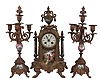 Clocks- 2 (Two) French Cast: (1) Japy Freres, Paris for Tiffany & Comp., three piece mantel garniture, 8 day, time and strike, spring-driven pendule de Paris movement in an ornate cast case with gold finish, painted porcelain panels signed "Carle" and matching candelabra, c1860; (2) France, figural clock, 8 day, time and strike with alarm, spring-driven pendule de Paris movement with in a gilt brass case cast in the form of a female figure holding a bird, all mounted on an ebonized wood base.