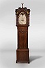 Charles Monks, Prescot, Lancashire, England, tall clock, 8 day, time and strike, weight driven movement in a Gothic revival mahogany case with reverse painted glass inserts above hood door, Gothic shaped trunk door over a base with framed panel on straight bracket feet. The painted metal dial has moon phase, seconds bit and calendar.