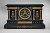 France, mantel clock, 8 day, time and strike, spring driven pendule de Paris movement with visible Brocot escapement in a black slate case with incised floral designs, gilt metal columns, and three classically inspired low-relief friezes depicting a crowd, chariot, soldiers, and an elephant, black slate dial with incised gold Roman numerals and gilt hands.