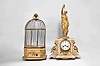 Clocks- 2 (Two): (1) France, figural mantel clock with conical pendulum, 8 day, time and strike, spring driven movement in a white stone case with applied gilt ornaments surmounted by gilt female figure holding pendulum aloft, white enamel dial with Roman numerals, and blued steel Breguet hands, c1880; (2) French, large singing bird cage, spring driven movement in a gilt wood and gesso base, brass cage, controls and winding from the base, c1880.
