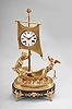 France, an unusual early 19th century gilt and patinated bronze figural clock, the oval base with four winged lion masks above paw feet, anthemion and palmette mounts, with central Medusa mask, and featuring two figures in a small sailboat, the rear with female figure, her left hand on the mast, and right hand holding what may be a torch, the bow with figure of cupid, his right hand raised, his left holding an anchor, the roman numeral white enamel dialmounted to tyhe sail, fancy gilt hands, two train pendule de Paris movement with silk thread suspension, striking on a bell, with associated oval base and dome