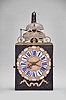 France, Comtoise clock, 8 day, time and strike with two bells, weight driven movement, verge escapement, thread suspension with rear-hanging pendulum in an iron post and plate frame, cast brass dial with two iron hands, floral motif and inset with 24 white enamel cartouche numerals, blue Roman numerals for the hours and black Arabic numerals every five minutes, flat brass winding arbor shutters below the dial, and pierced brass fronton.