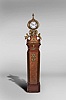 Marti & Cie, Paris, France, figural shelf clock, 8 day, time and strike, spring driven movement with white enamel dial in a highly stylized cast brass case set on veneered wooden base surmounted by three putti grasping bacchanal themed items and cast brass appliques including matching stand with cast brass appliques, veneers and ornaments.