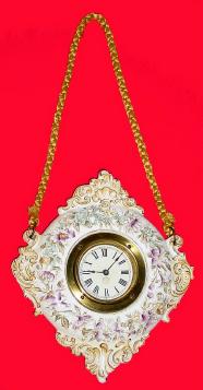 New Haven Clock Co., "San Remo" hanging porcelain thirty-hour timepiece. Case is in perfect condition and floral decorations and gilt work are exceptionally well preserved. Dial has been very skillfully repapered with New Haven trademark applied. Hands are original. — Antique Clocks Price Guide