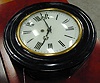 A BLACK PAINTED AND ENAMEL WALL CLOCK.